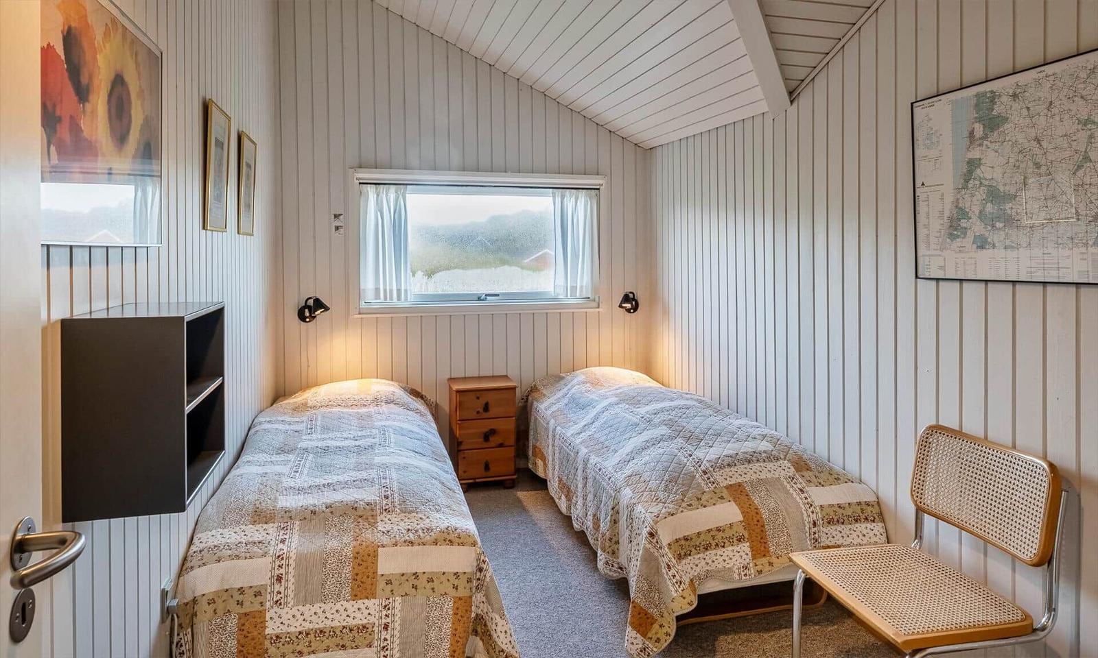 Zwei Betten mit gemusterten Bettdecken, Schreibtisch, Stuhl und Fenster mit Blick nach draußen.