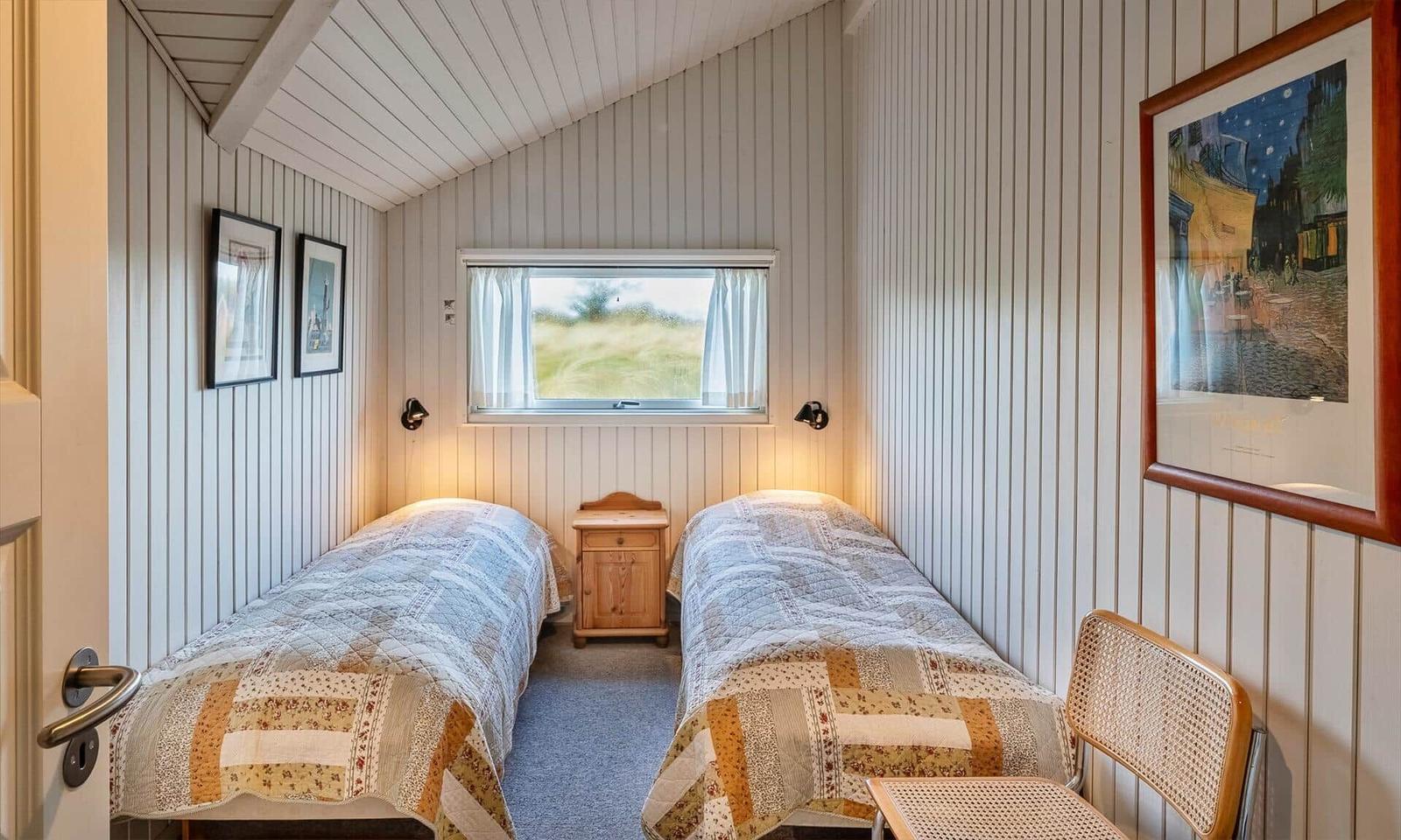 Zwei Betten mit gemusterten Decken, kleiner Nachttisch und Fenster mit Blick auf Gras.