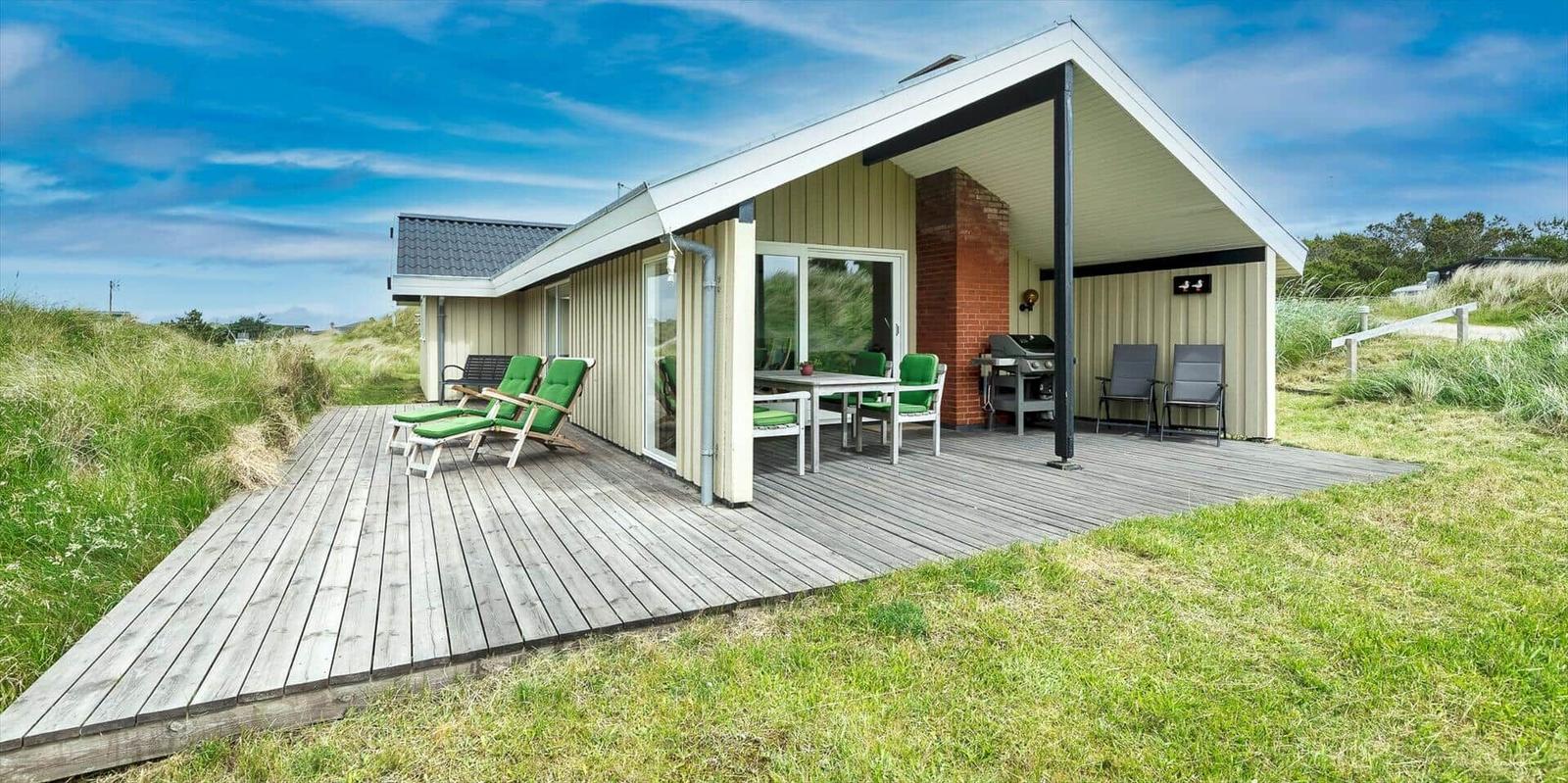 Haus mit Holzterrasse, Grill und grünen Stühlen im Freien.