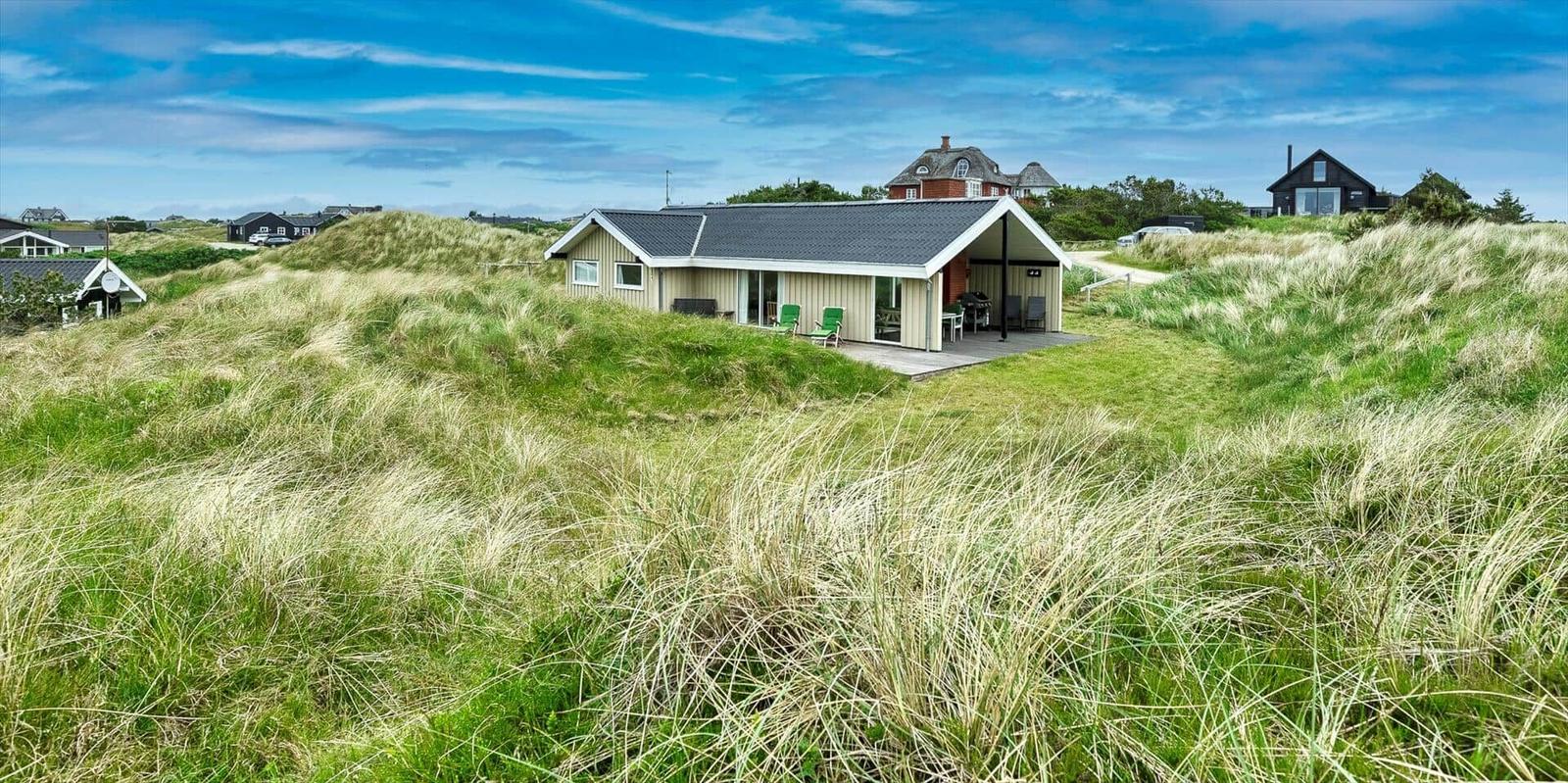 Ein modernes Haus mit Terrasse liegt in grünen Dünen.