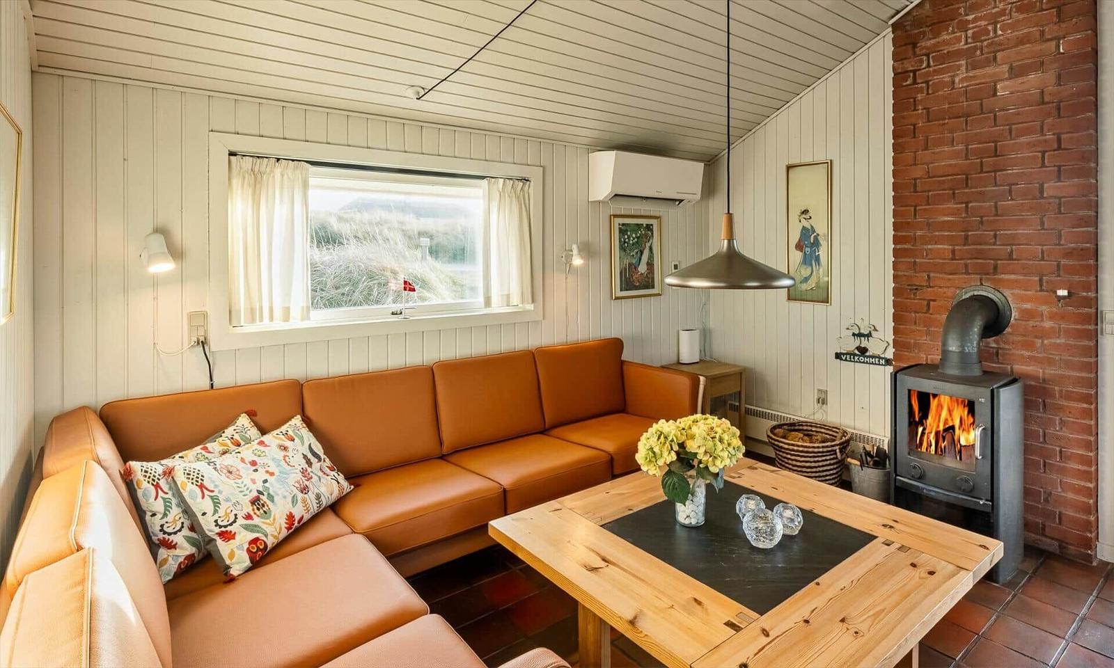 Wohnzimmer mit braunem Sofa, Holztisch und Kaminofen an Backsteinwand.