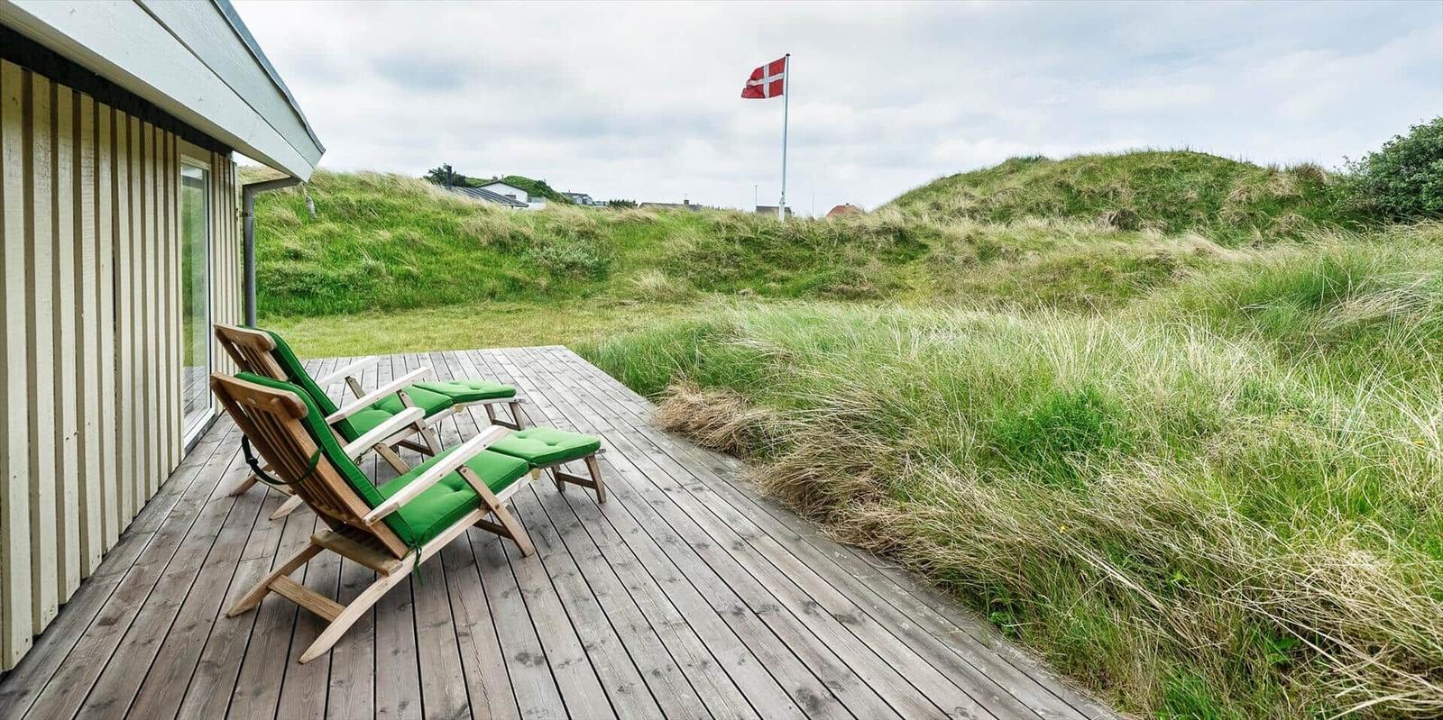 Terrasse mit zwei grünen Liegestühlen, Blick auf Grasland und dänische Flagge.