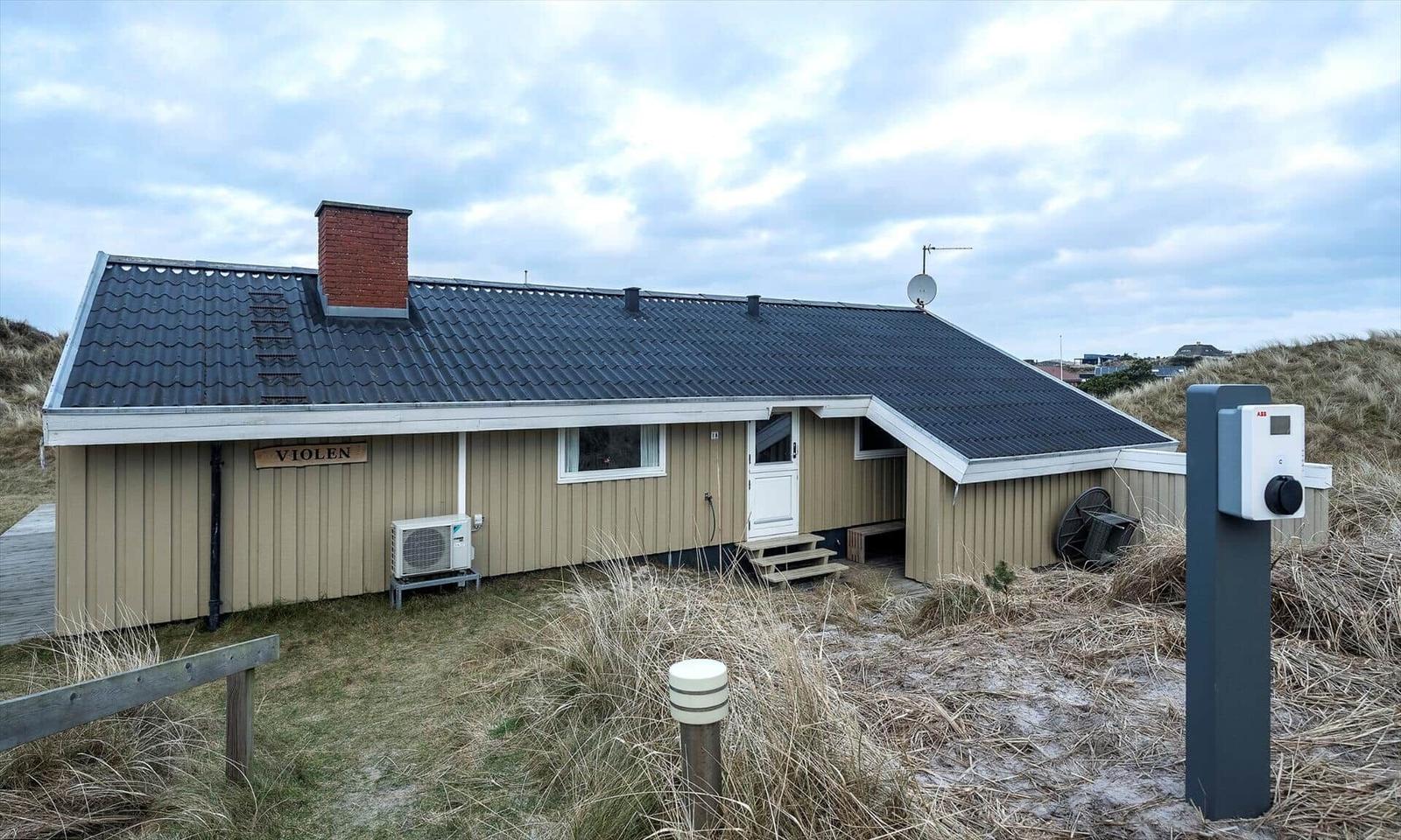 Einhaus mit dunklem Dach und hellen Wänden, umgeben von Dünen und Gras.