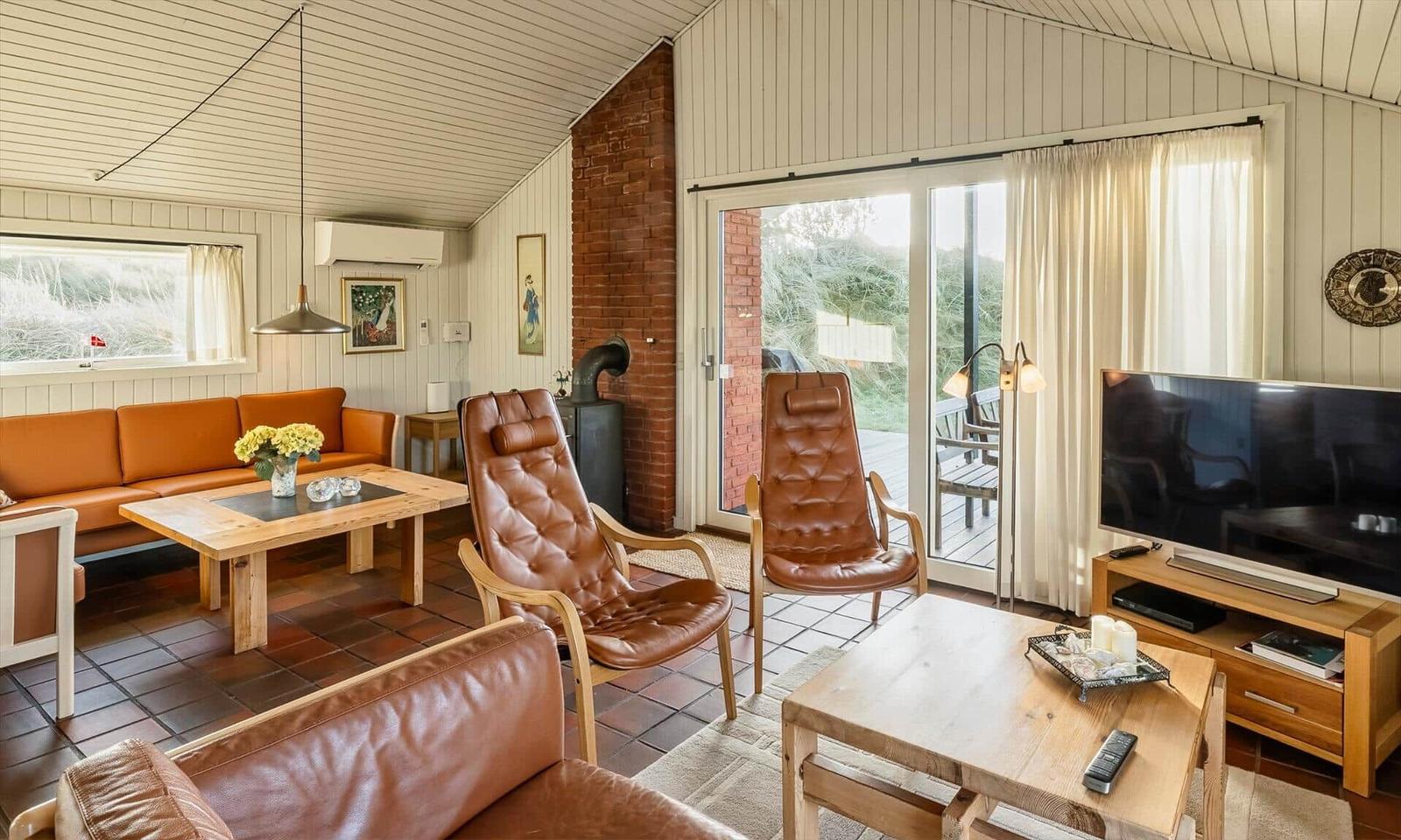 Wohnzimmer mit braunen Ledermöbeln, Holztischen und Blick auf Terrasse.