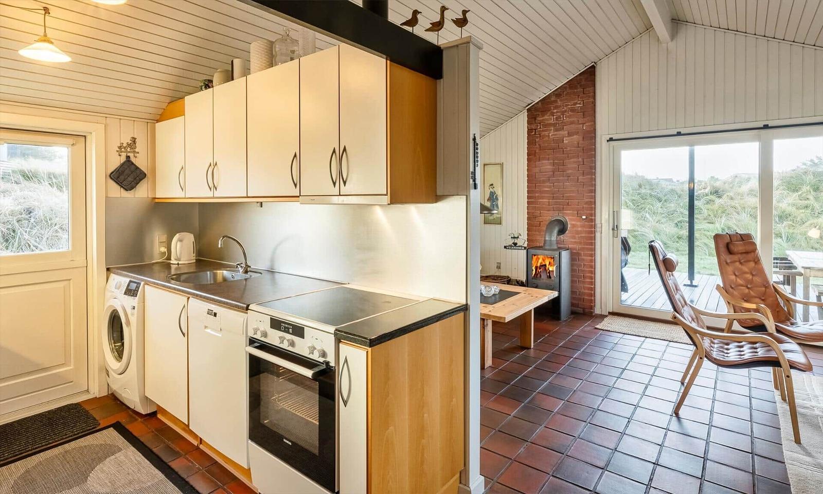 Küche mit Spüle, Herd und Waschmaschine. Wohnbereich mit Kamin und Sitzgelegenheiten.