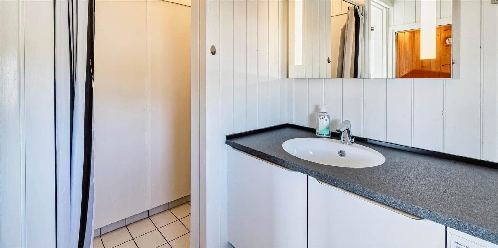 Waschbecken mit Spiegel und Seifenspender an grauem Arbeitsplatz.