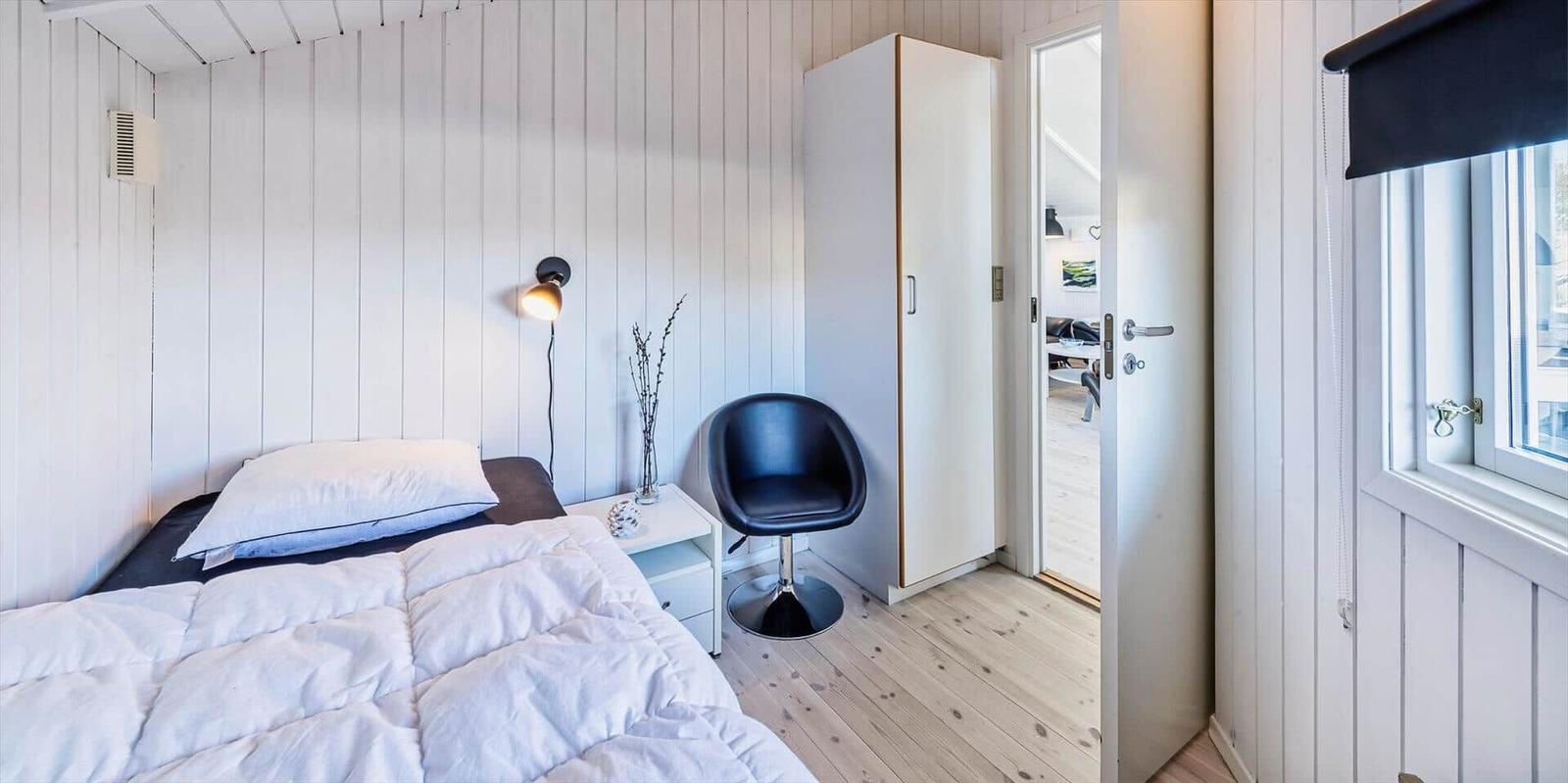 Schlafzimmer mit Bett, Stuhl und Kleiderschrank. Fenster mit Rollladen und Tür zum Flur.