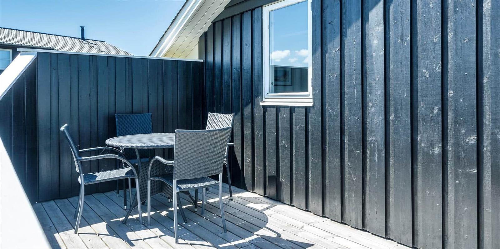 Terrasse mit Tisch und Stühlen vor schwarzem Holzhaus