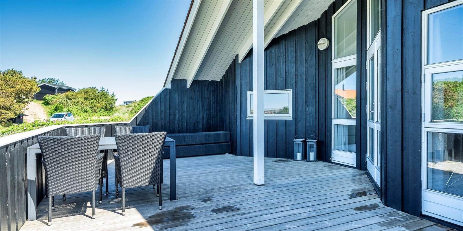 Terrasse mit Tisch, Stühlen und Sitzbank. Dunkelblauer Holzaufbau mit Glasfronten.