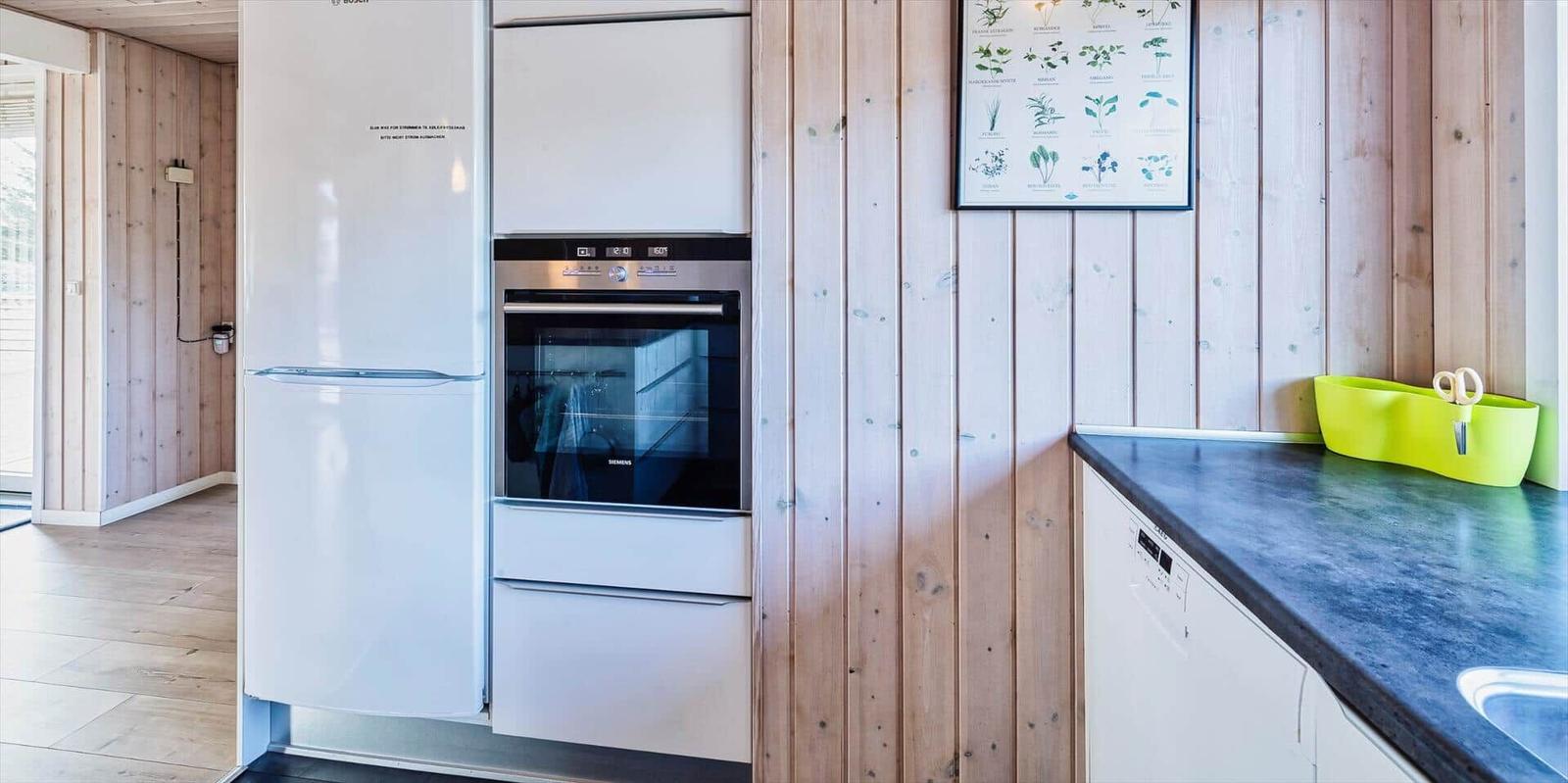 Küche mit Kühlschrank, Backofen und Waschmaschine an Holzwand
