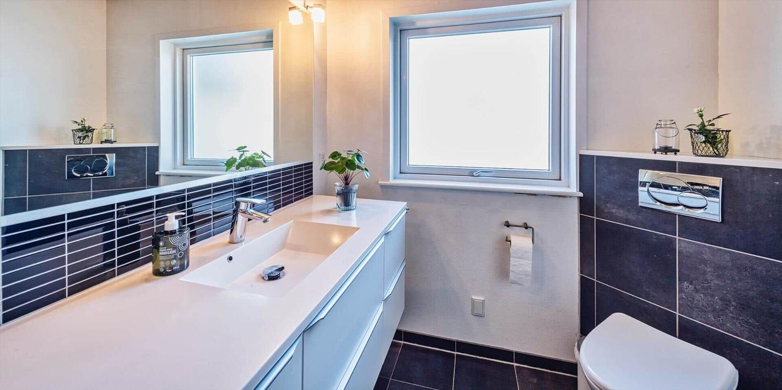 Badezimmer mit Waschbecken, Spiegel, Toilette und Fenster