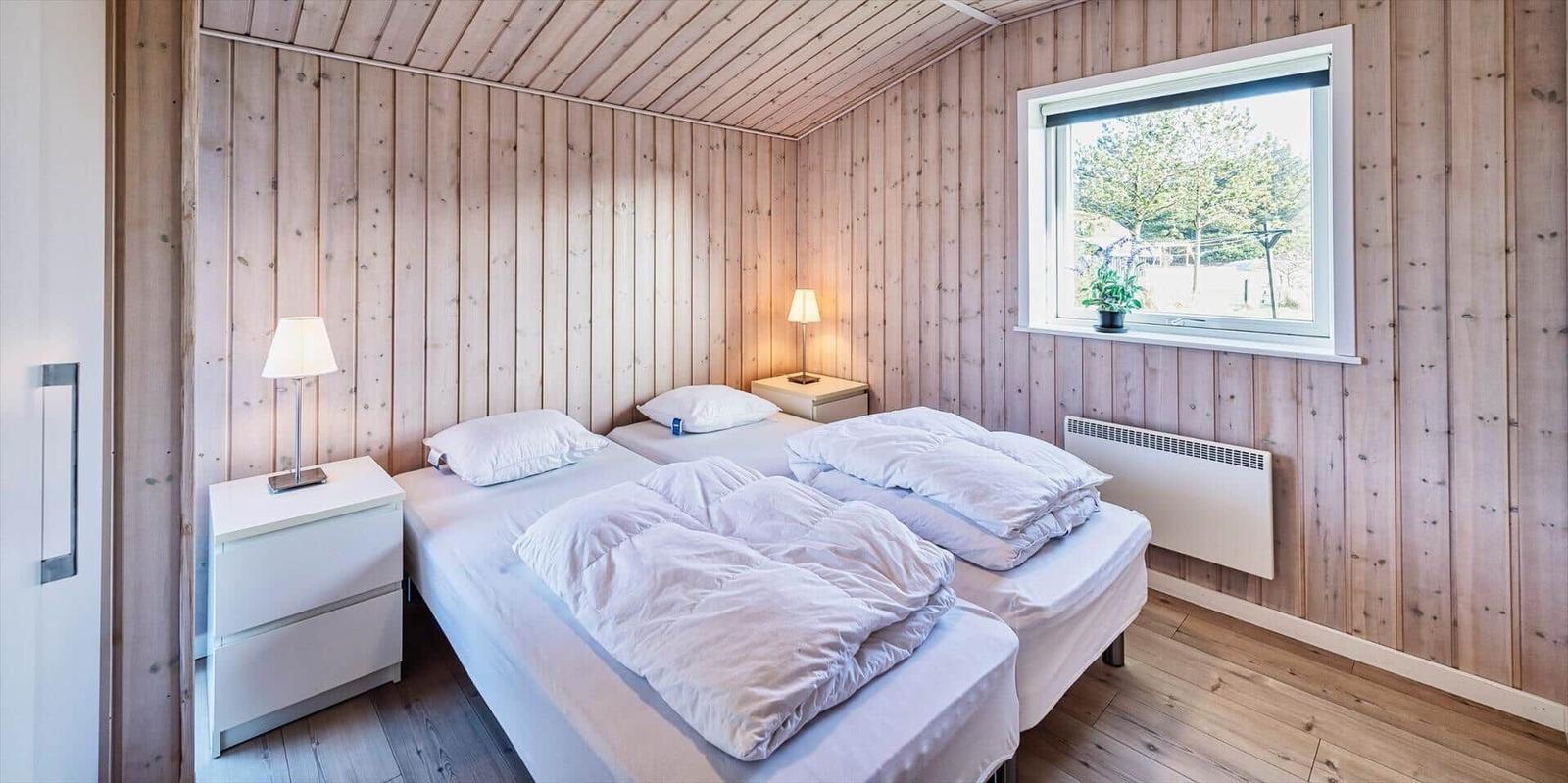 Zwei Betten mit weißen Bettwäschen, Holzwand und Fenster mit Blick auf Bäume.
