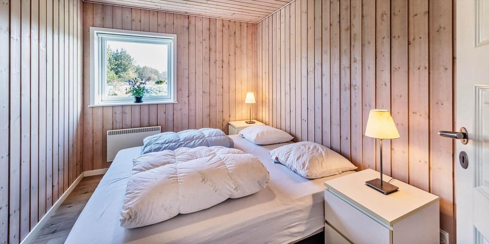Schlafzimmer mit Holzwand, Bett, Nachttisch und Fenster mit Blick auf Grün.