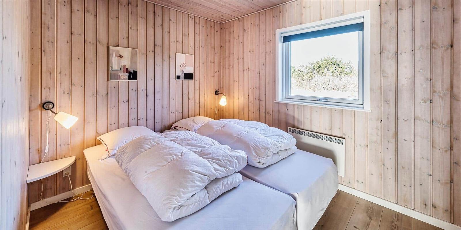 Schlafzimmer mit Holzwänden, Doppelbett und Fenster mit Blick auf Grünflächen.