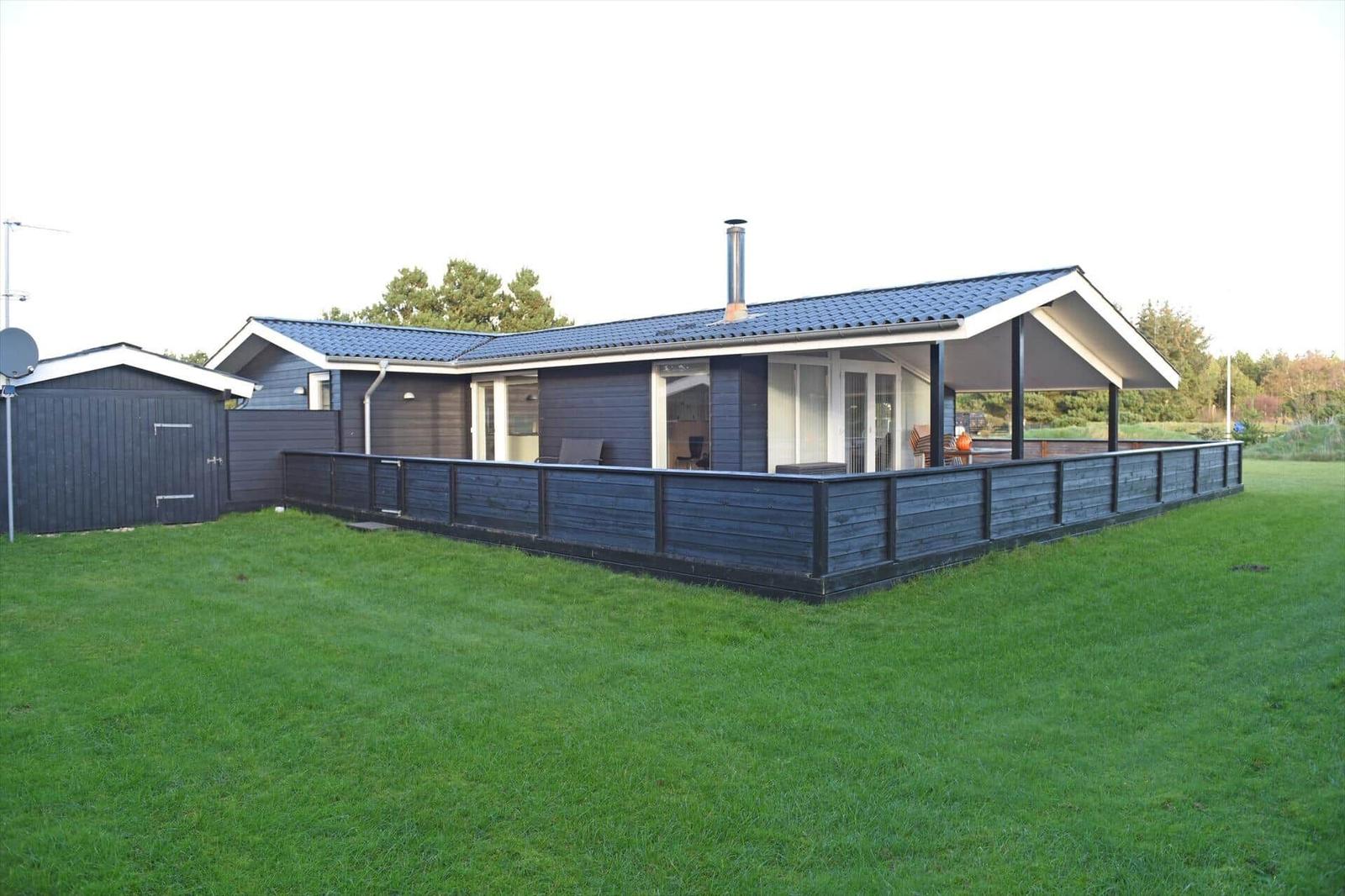 Moderne Ferienhaus mit Terrasse und Garten. Schwarze Holzverkleidung und blauer Dachziegel.
