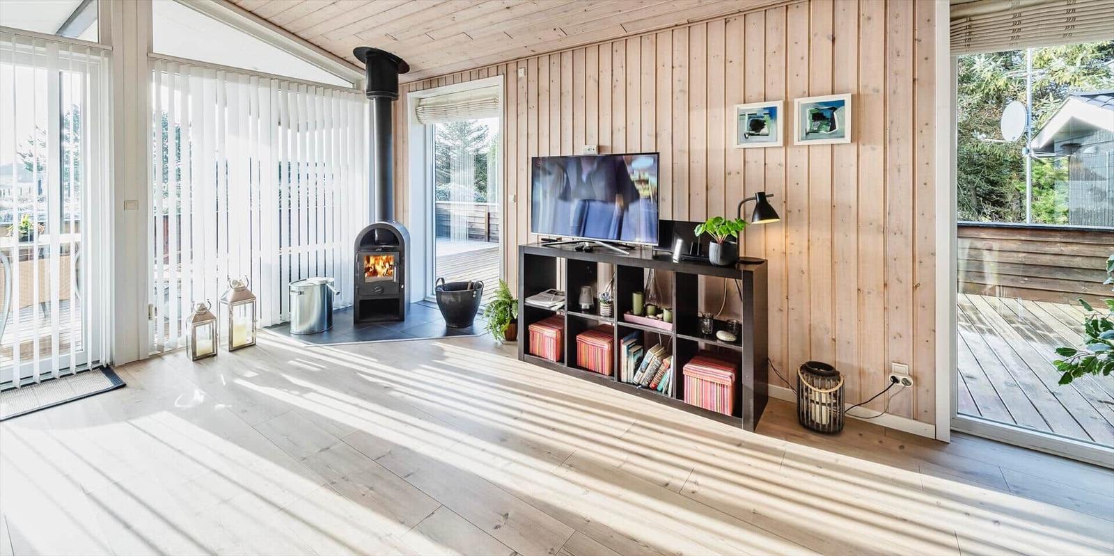 Wohnzimmer mit Holzwand, Kamin und TV-Bereich. Holzdielenboden und große Fenster.