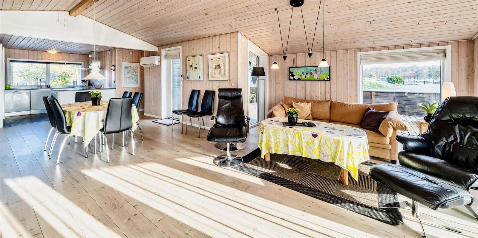 Wohn- und Essbereich mit Holzboden, Sofa, Essgruppe und Sessel. Küche im Hintergrund.