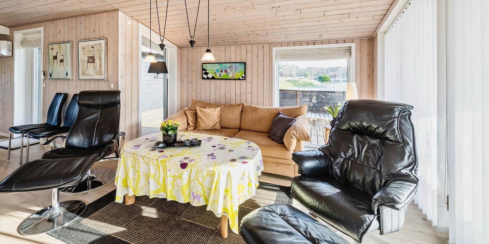 Wohnzimmer mit braunem Sofa, schwarzen Ledersesseln und runden Tisch mit Tischdecke.
