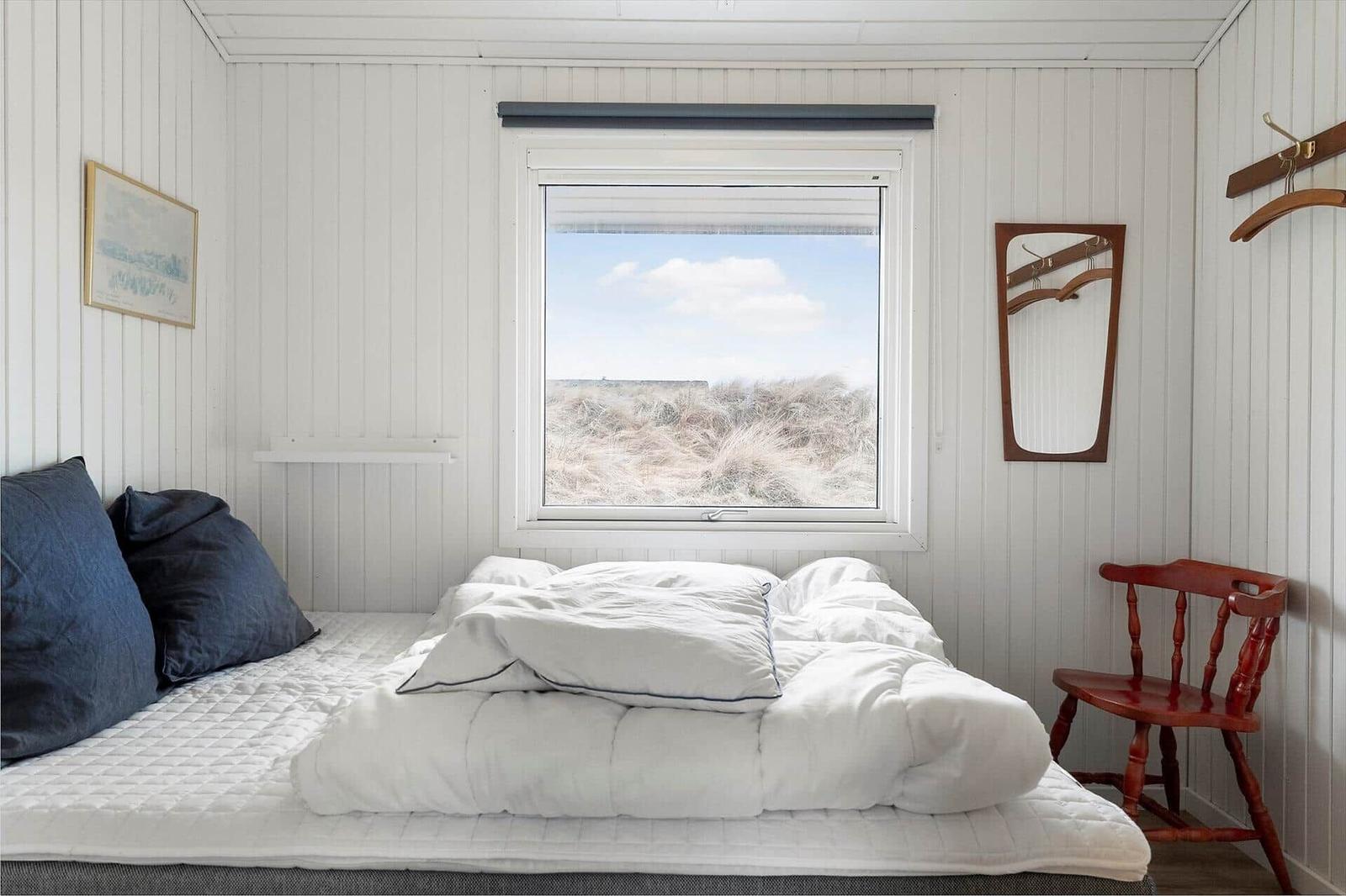 Schlafzimmer mit Bett, Fenster und Holzstuhl.