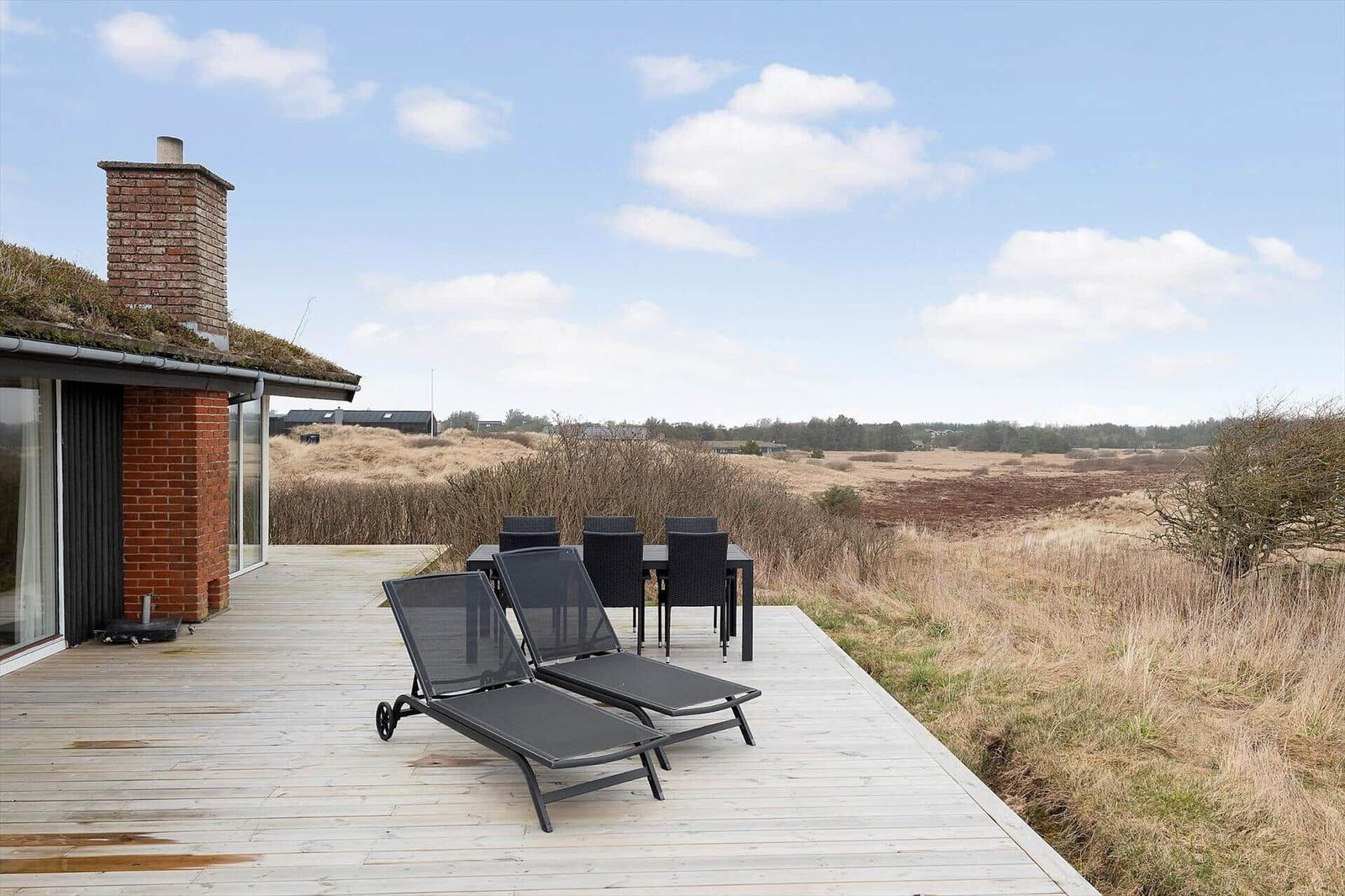 Terrasse mit Liegestühlen und Esstisch. Blick auf trockenes Gras und Himmel.