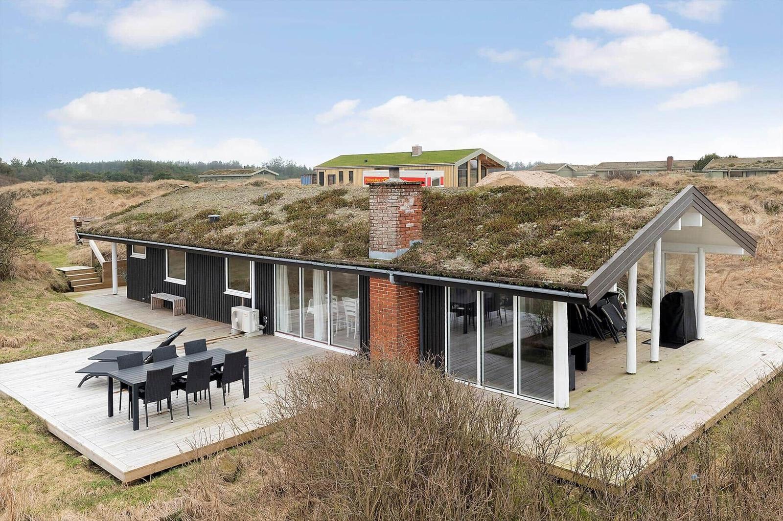 Moderne Villa mit Grasdach und Holzterrasse. Gartenmöbel und große Fenster.