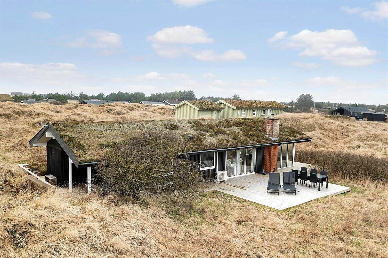 Moderne Strandhaus mit grünem Dach und Terrasse im Dünenland.