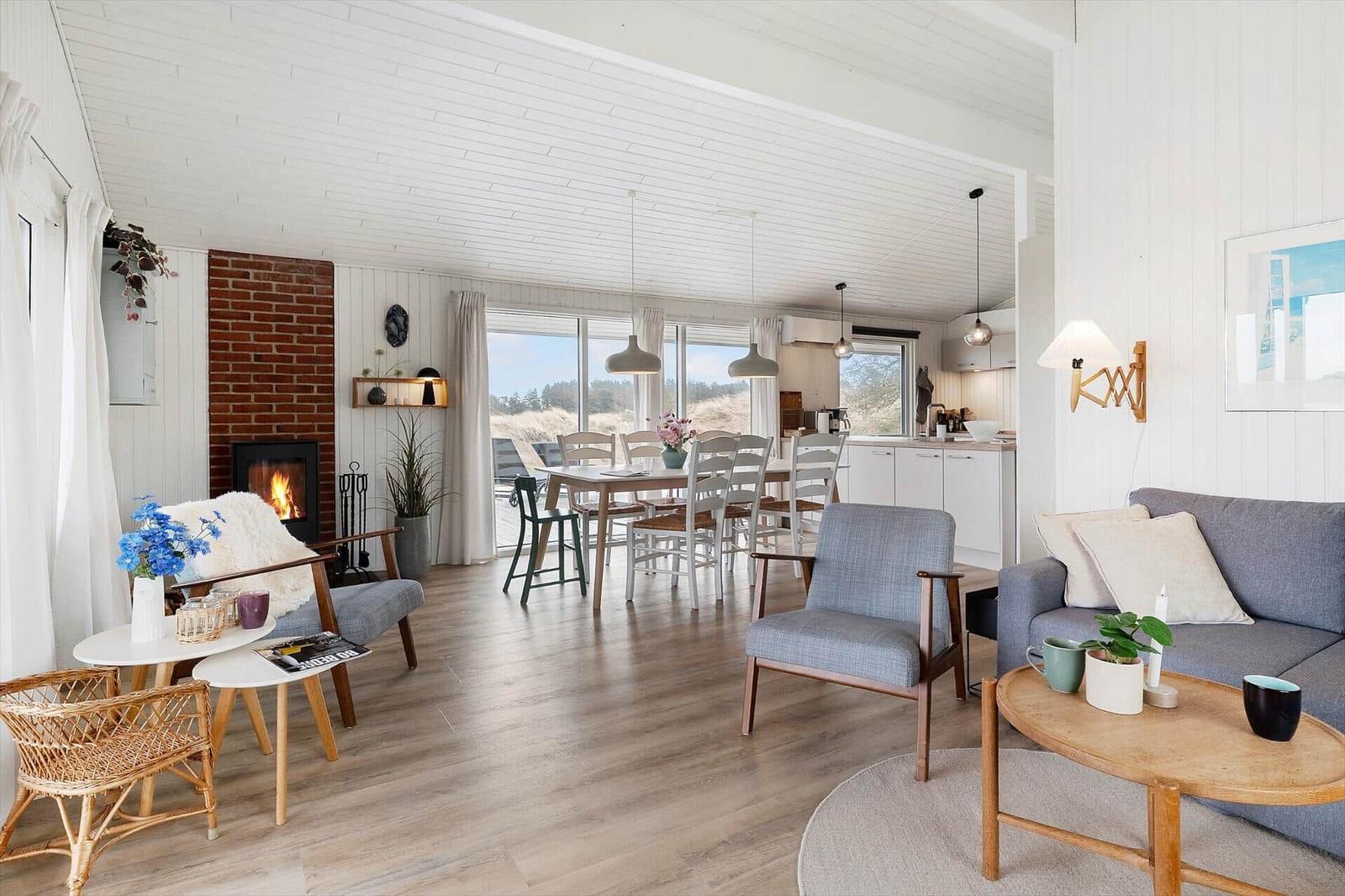Wohn- und Essbereich mit Kamin, Tisch und Stühlen, Sofa und Couchtisch. Holzboden und große Fenster.
