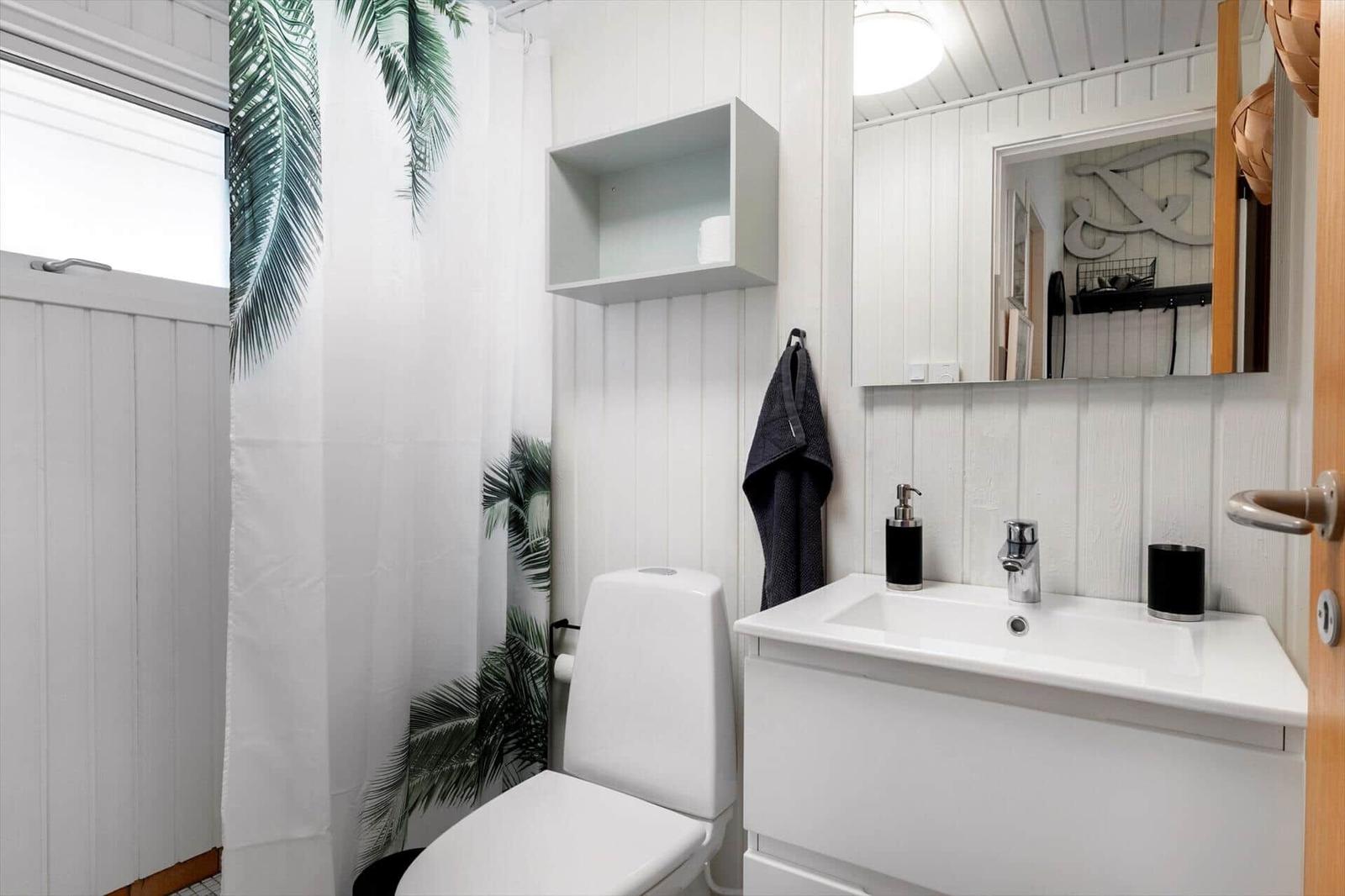 Badezimmer mit Toilette, Waschbecken und Duschvorhang mit Palmenmuster.