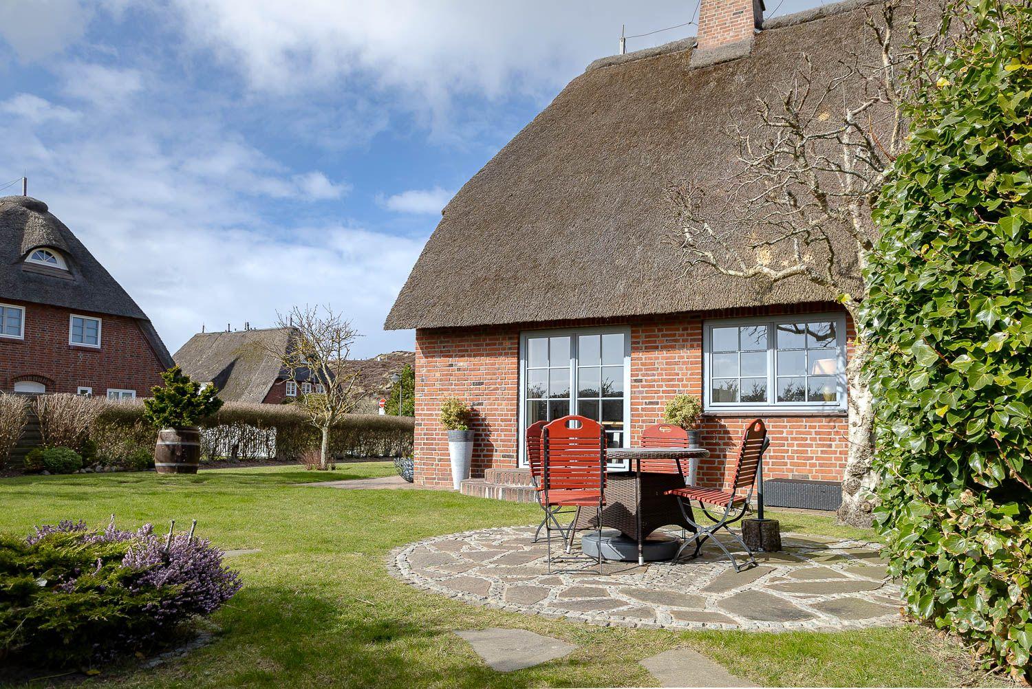 Haus mit Strohdach, Garten und Terrasse mit Tisch und Stühlen.