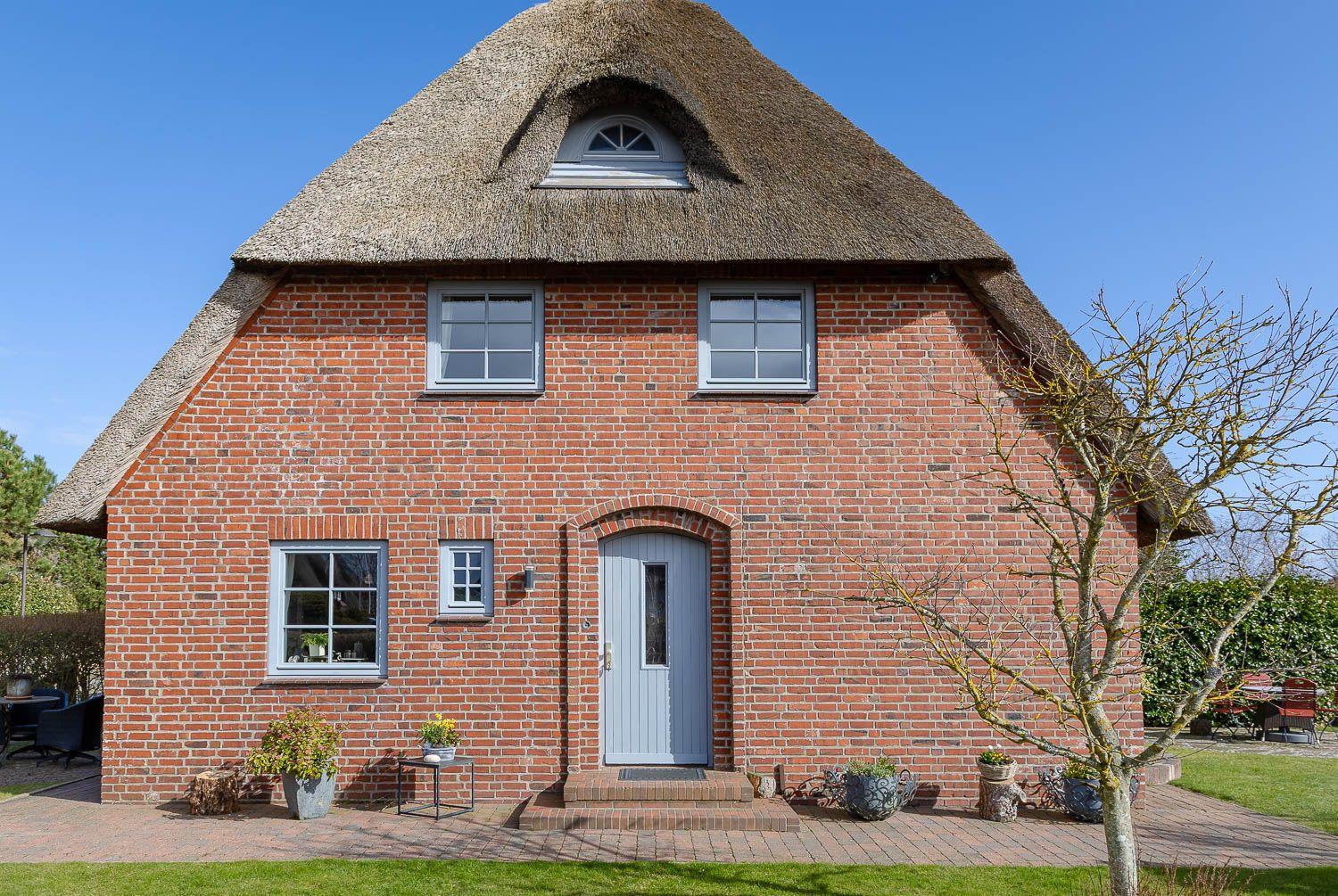 Rotes Backsteingebäude mit Strohdach und blauer Tür.