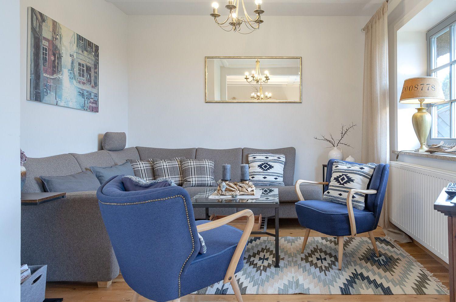 Wohnzimmer mit grauem Sofa, zwei blauen Sesseln und gemustertem Teppich.