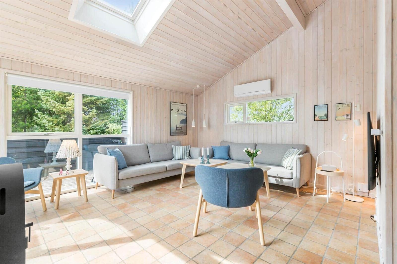 Living room with wood walls, sofa, chairs, and window view of trees.