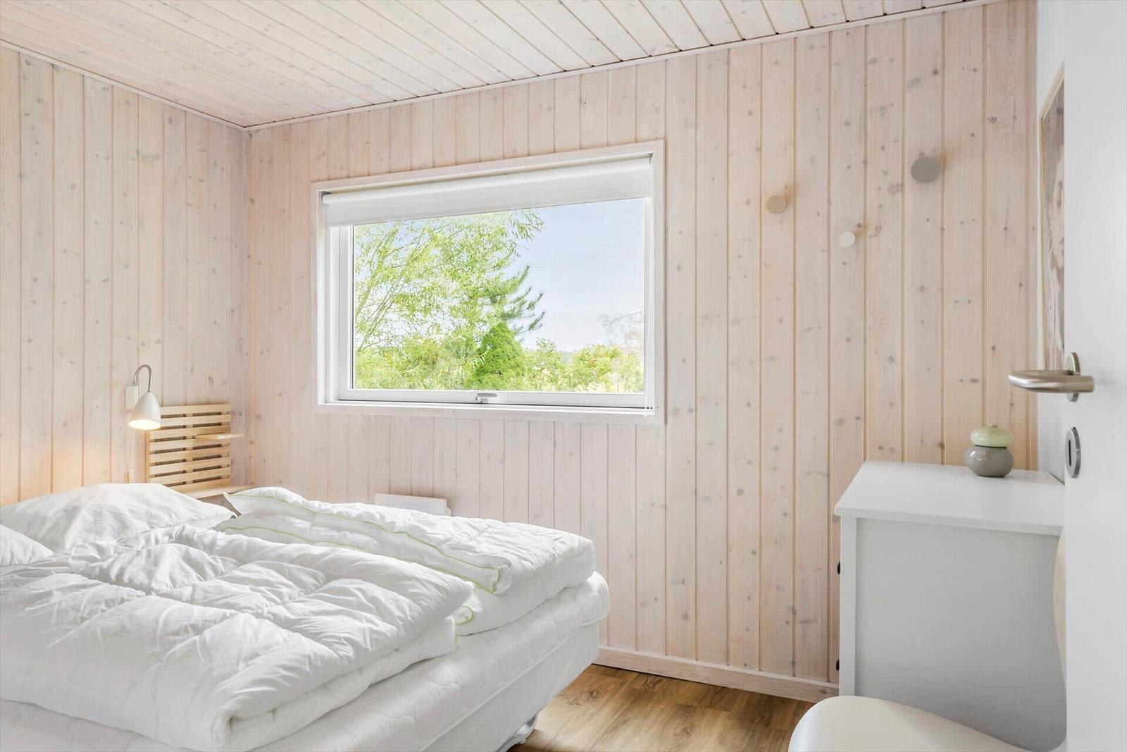 Bedroom with wooden walls, bed, and window with view of trees.