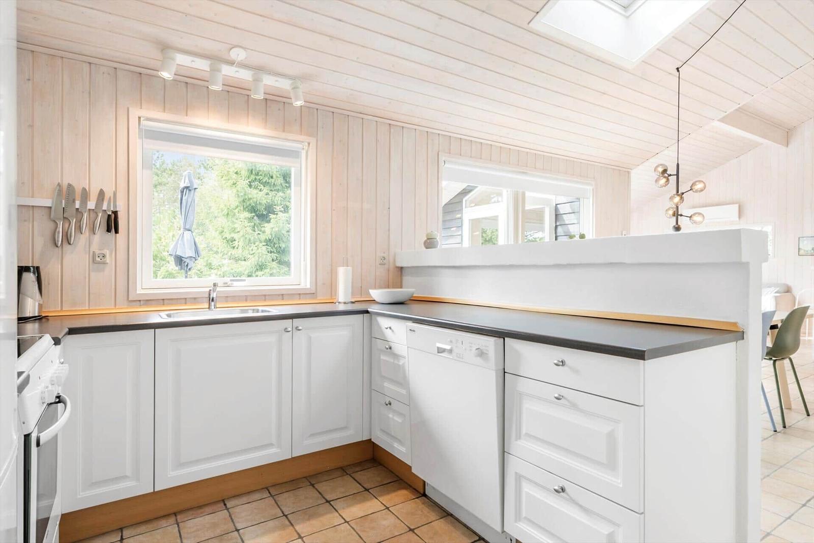 Kitchen with white cabinets, dark worktop, and wooden wall. Windows with garden view.