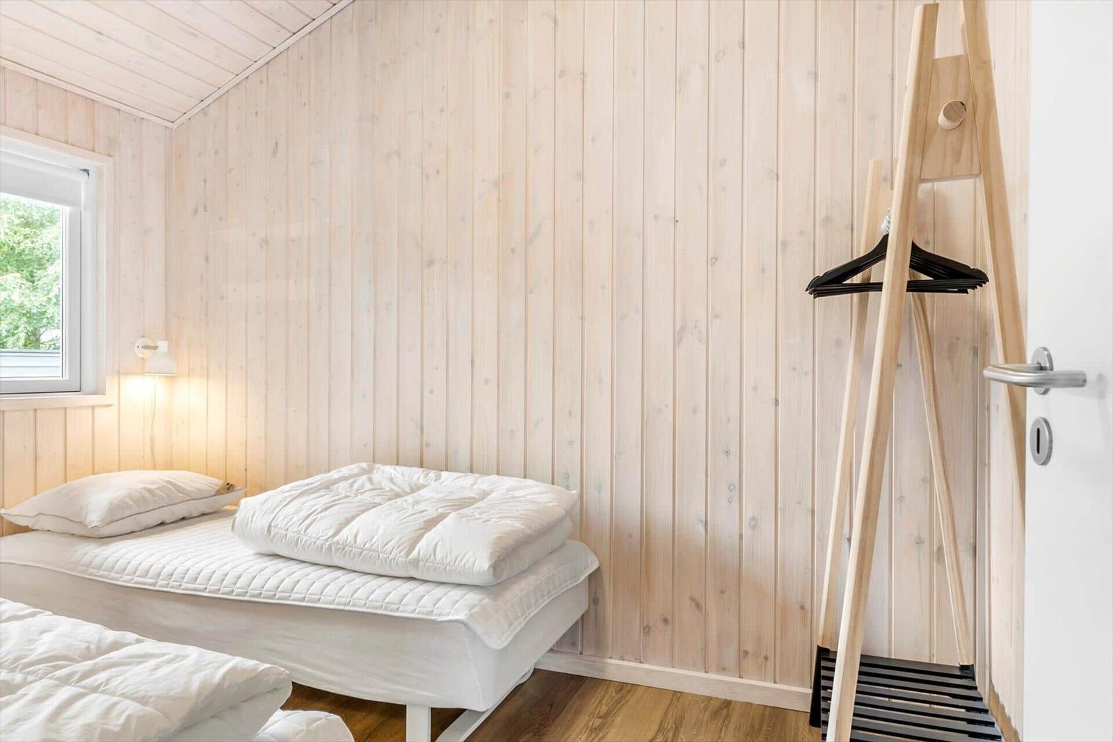 Room with wooden walls, bed, window, and coat rack.