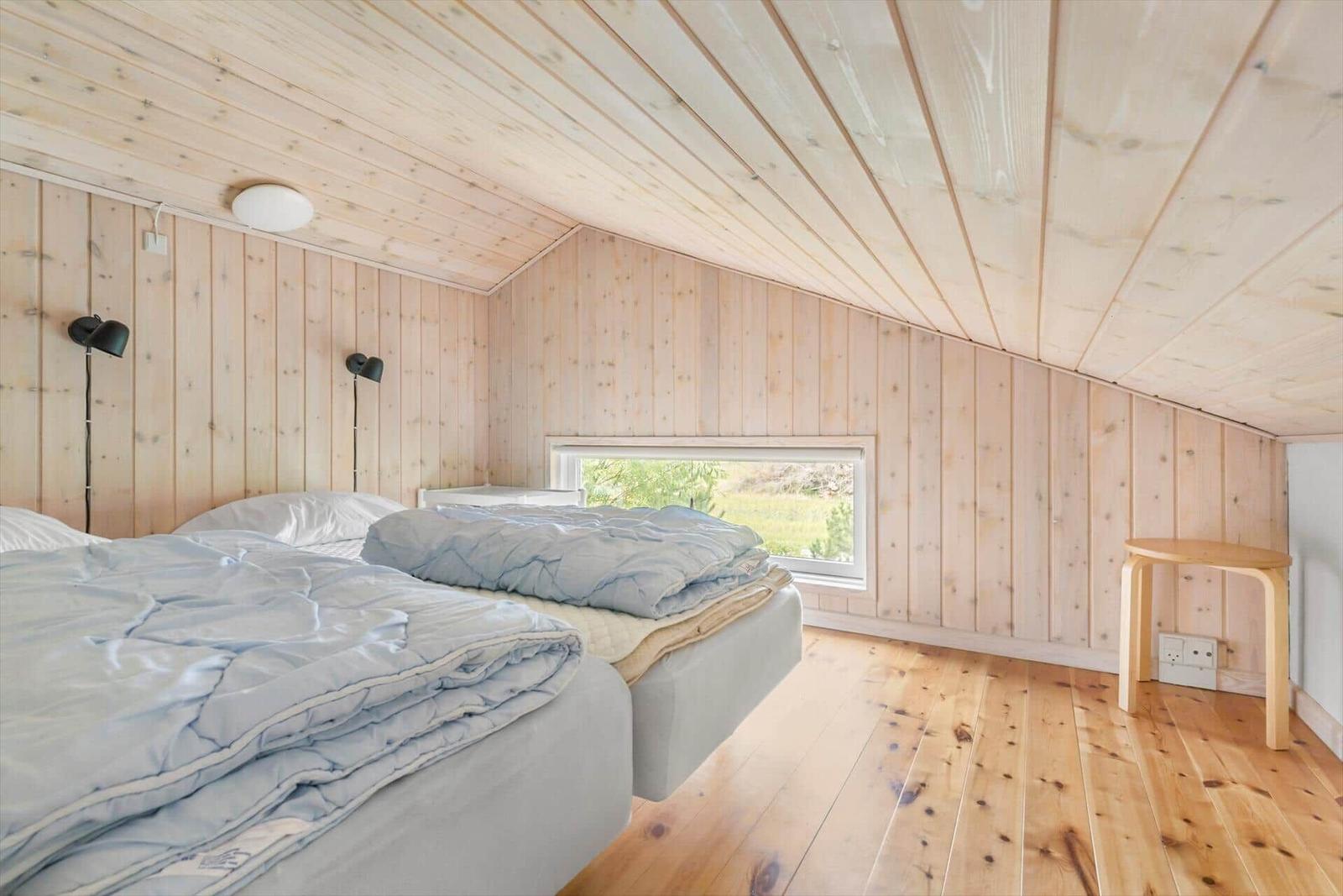 Two beds in a wooden house with sloped ceilings and window view.