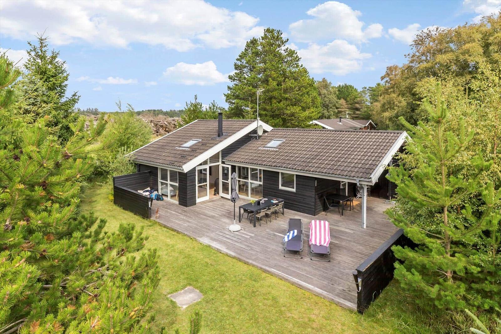 Modern wooden house with large deck and garden in green surroundings.
