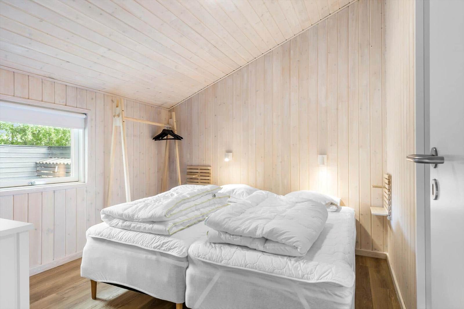 Bedroom with two beds, wooden walls, and window view.