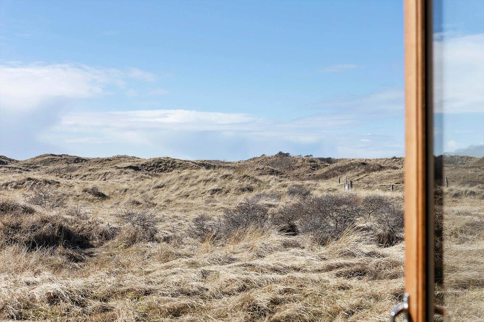 View of dry grassland and hills under blue sky through window
