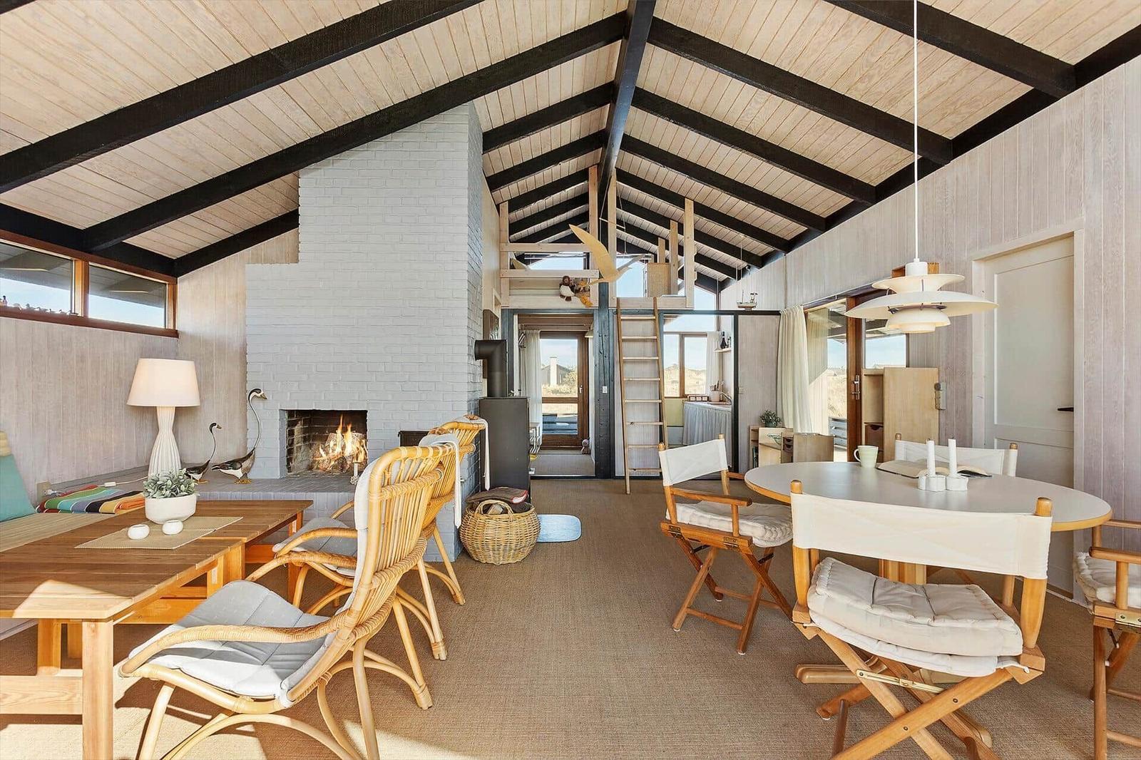 Living area with fireplace, dining table, and seating under wooden ceiling.