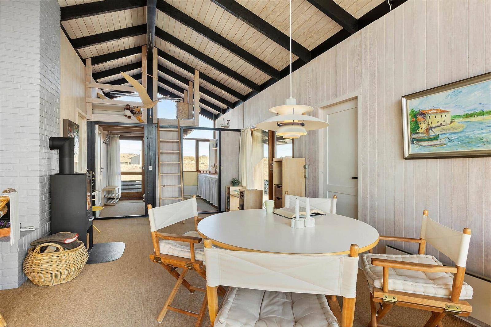 Round table with chairs, fireplace, and wooden ceiling in living area.