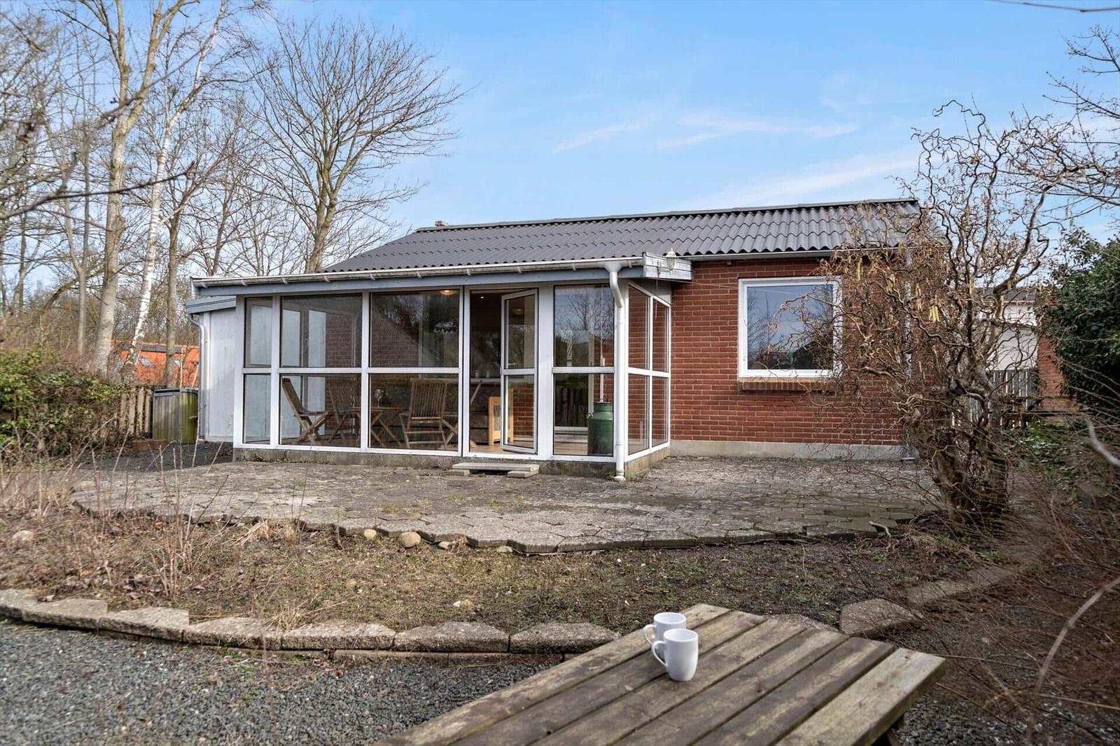 Haus mit Glasveranda, Terrasse und Garten. Holztisch mit zwei Tassen.