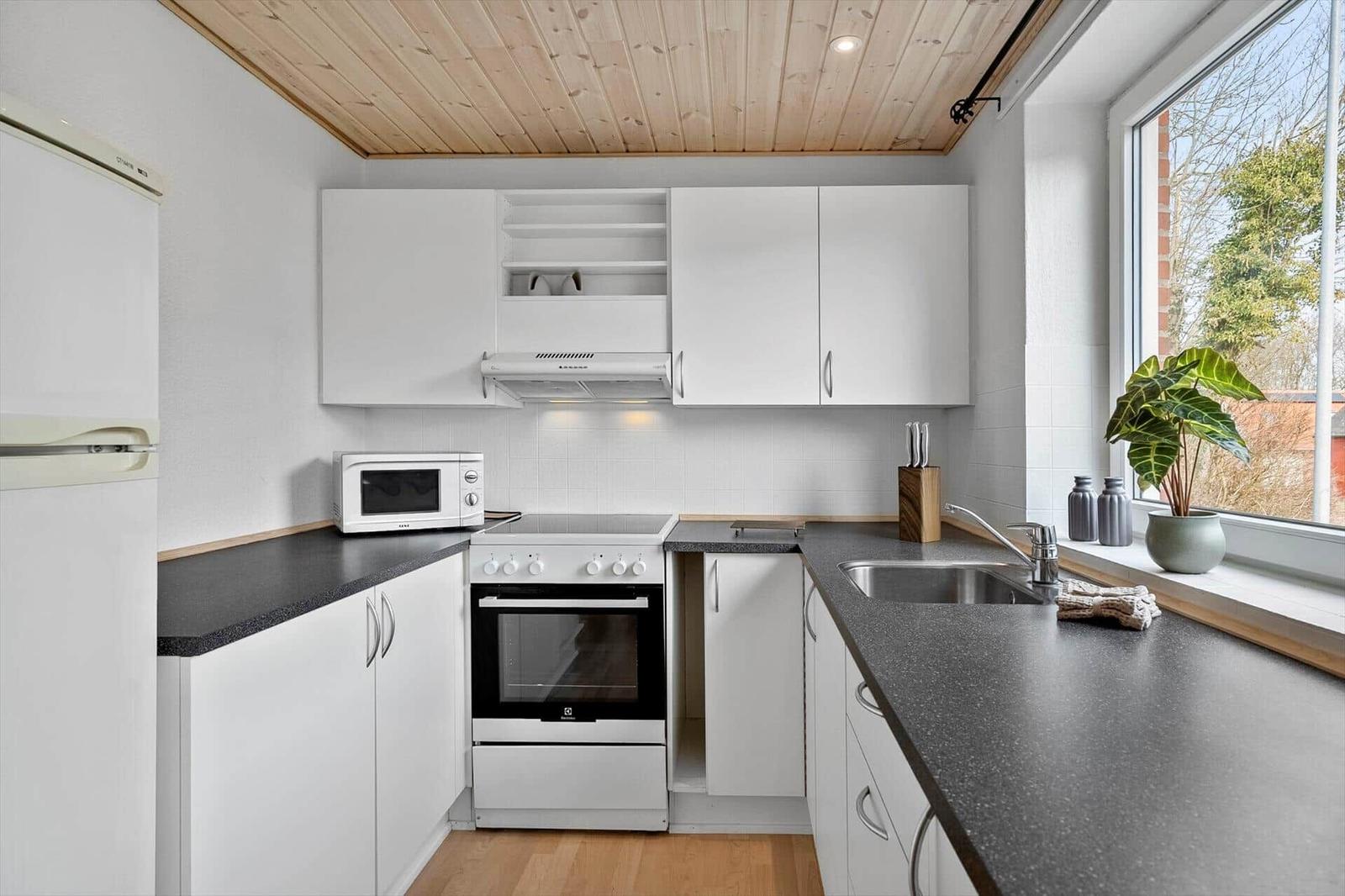 Küche mit weißen Schränken, dunklem Arbeitsplatz und Holzdecke.