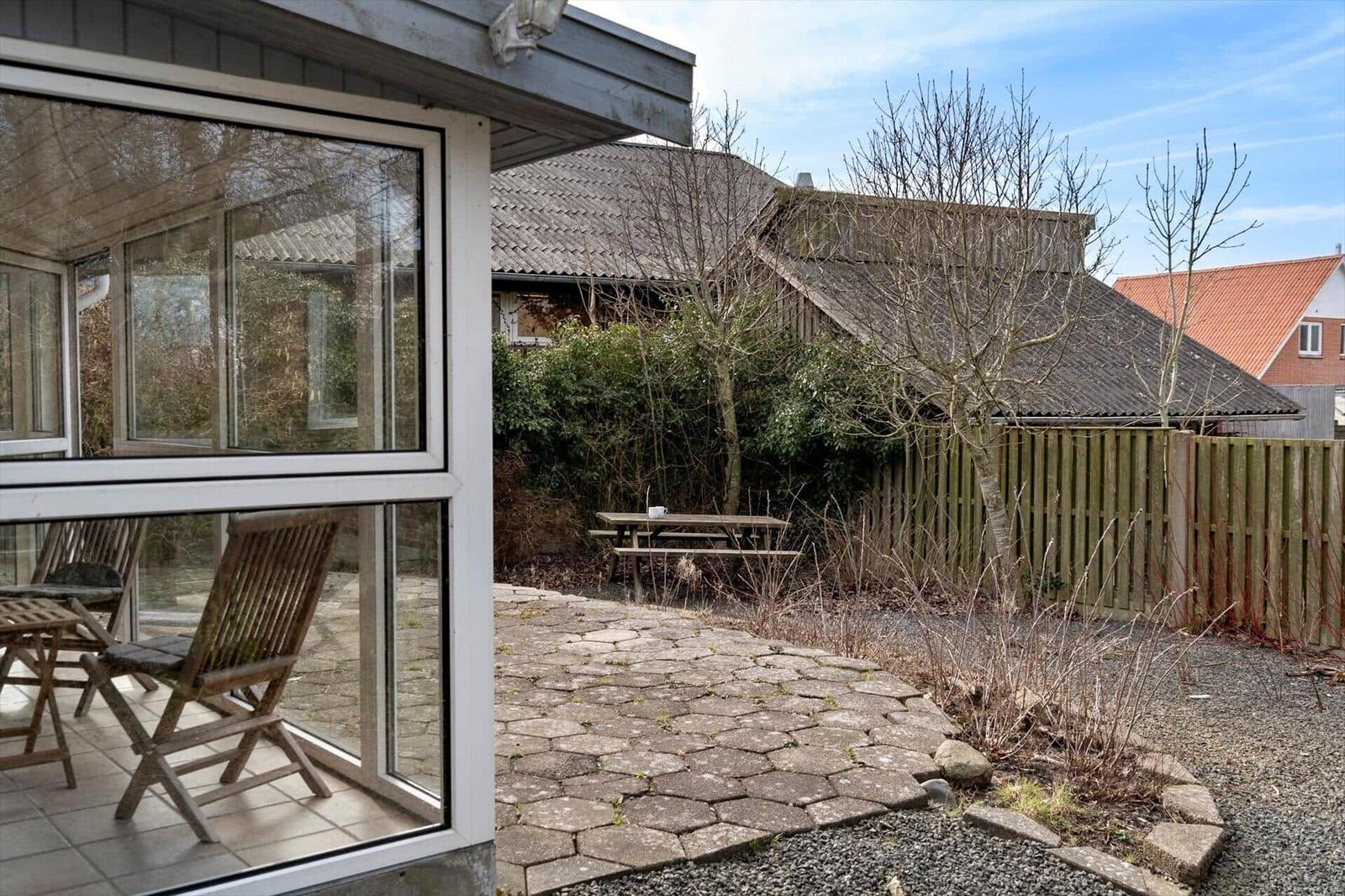 Hinterhof mit Steinplatten, Holzbank und Zaun. Durchgehendes Glasdach über Terrasse.