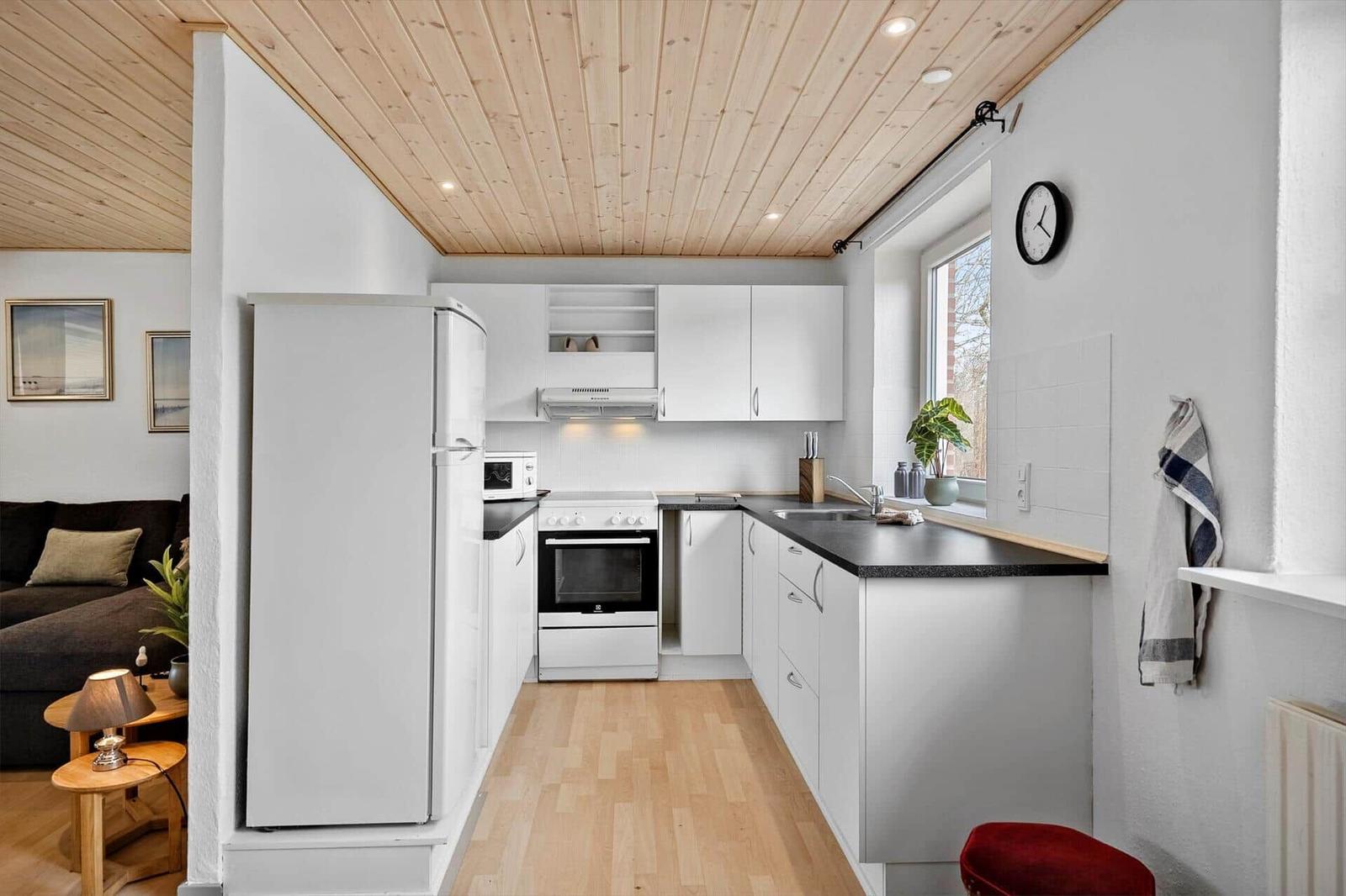 Küche mit weißer Einbauküche, Kühlschrank, Herd und Fenster