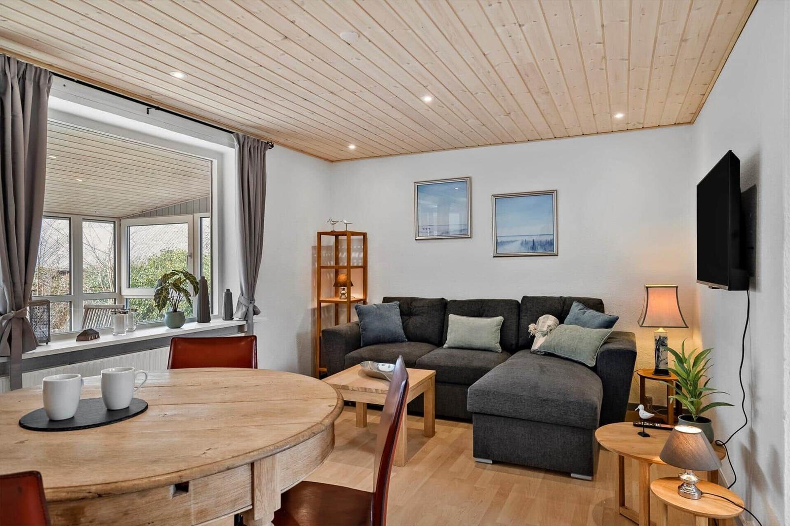 Wohn- und Essbereich mit Sofa, Tisch und TV. Holzdecke und Fenster mit Blick.