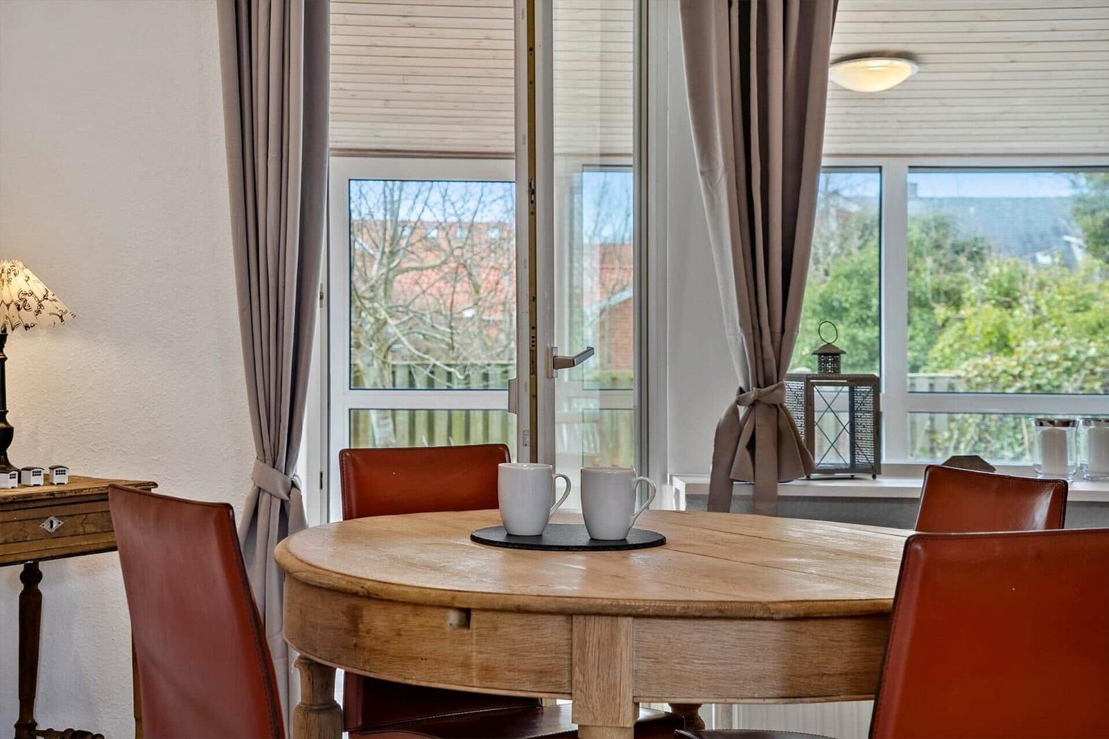 Rundes Holztisch mit vier roten Ledersitzen und zwei Tassen vor großem Fenster.