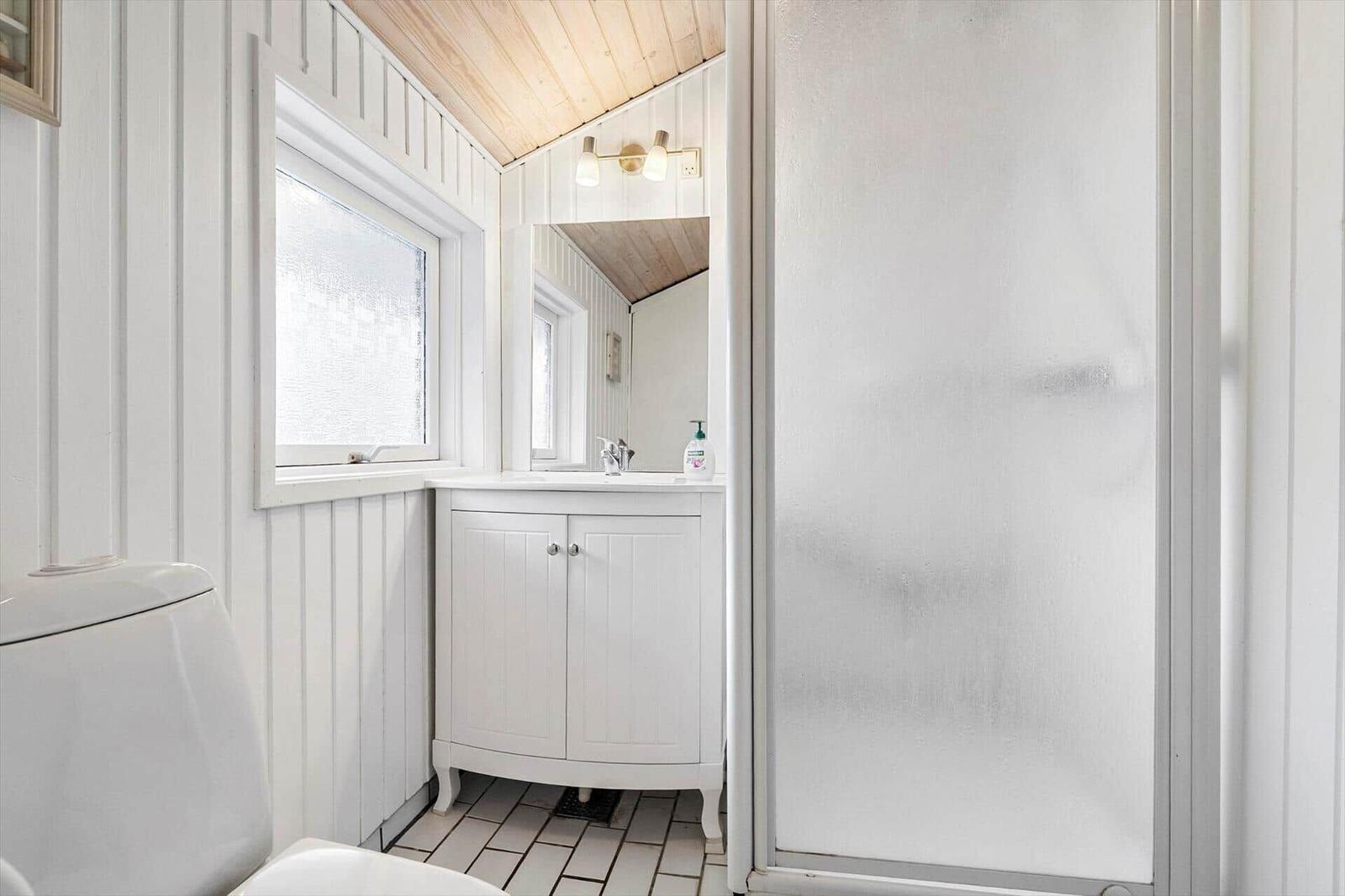 Badezimmer mit Dusche, Waschbecken und Toilette. Weiße Wände und Holzdecke.