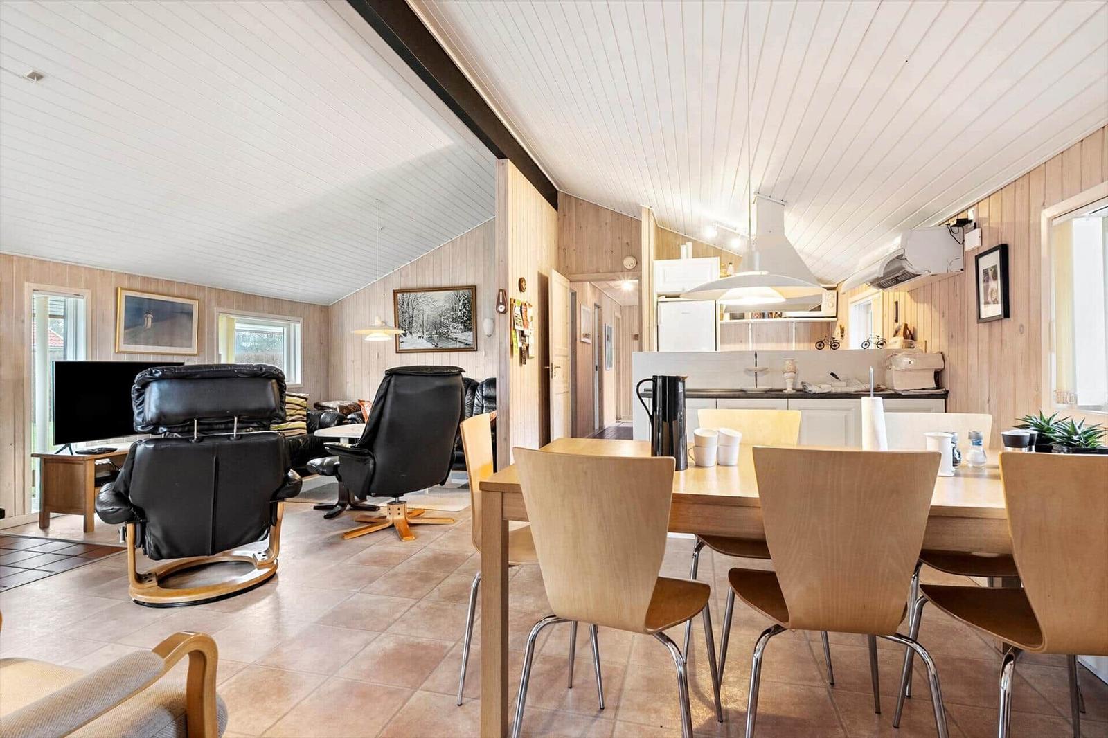 Essbereich mit Holztisch und Stühlen. Im Hintergrund Küche und Wohnbereich mit Ledersofas.
