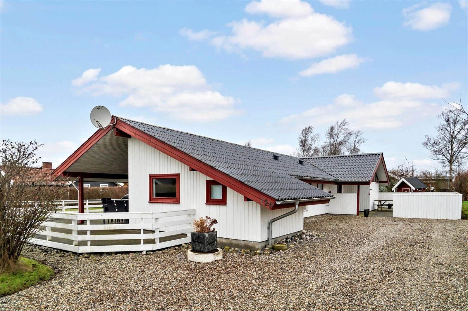 Wohnhaus mit Terrasse, Satellitenschüssel und Kiesfläche. Rote Fensterrahmen und weiße Wände.